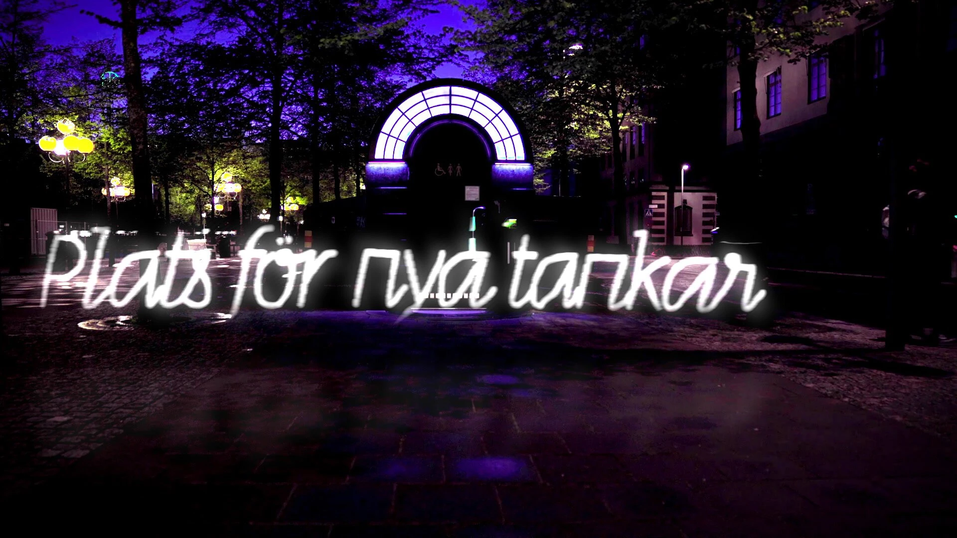 Plats för nya tankar, written in white script light across a dark courtyard below a lit arched gateway.