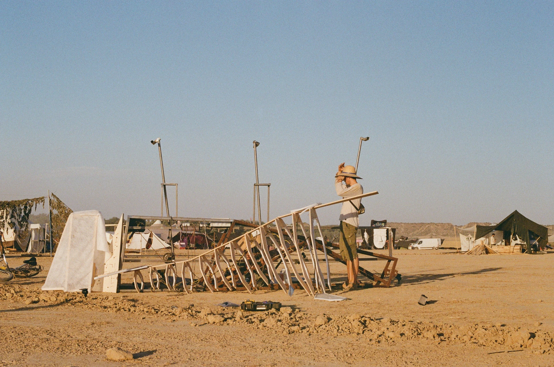 A film photograph of the whale's ribs and mechanical frame laid out for assembly in the desert, with a crew member standing beside them.