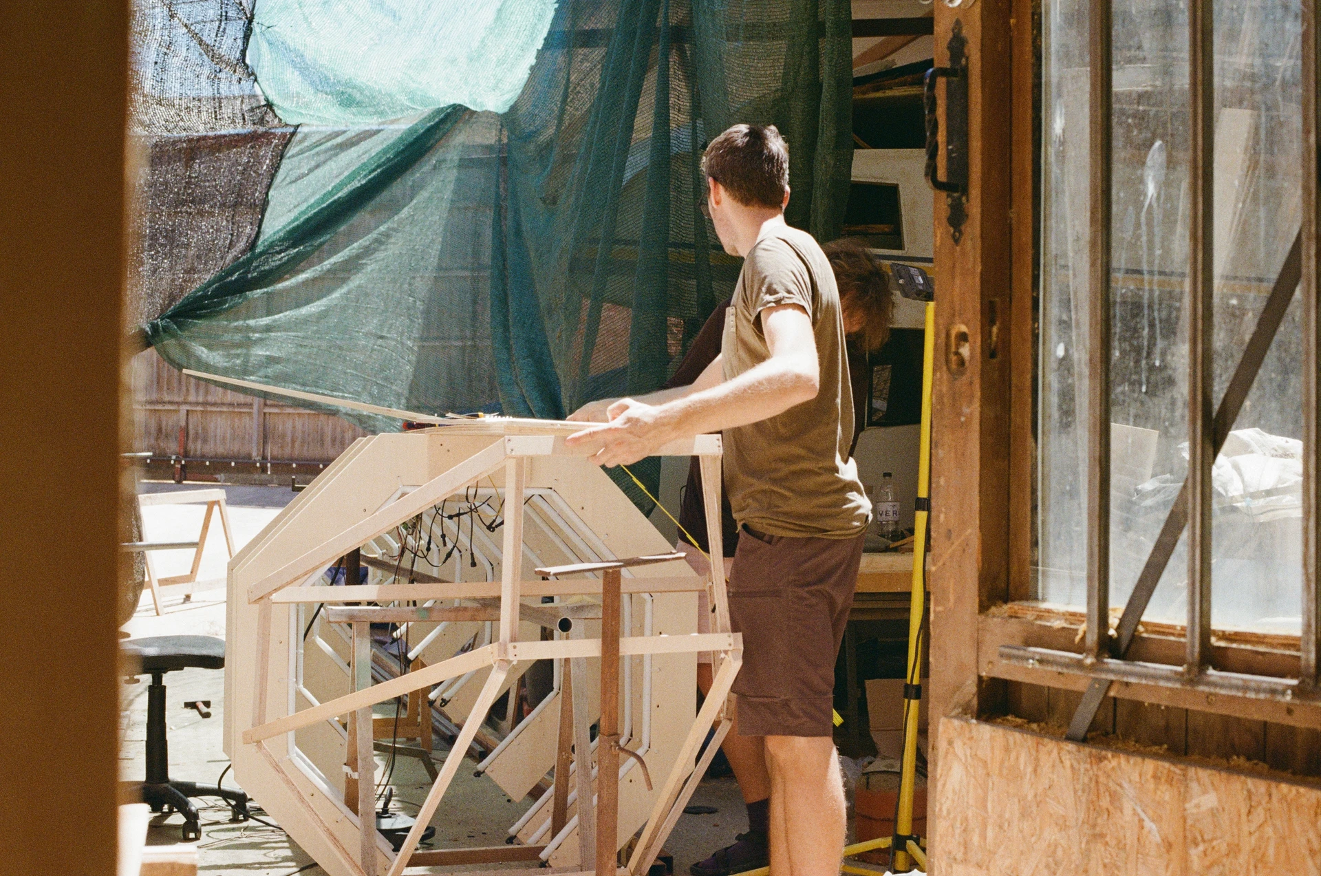 A film photograph of the whale being assembled in a workshop, with its wooden ribs supported on a metal frame.