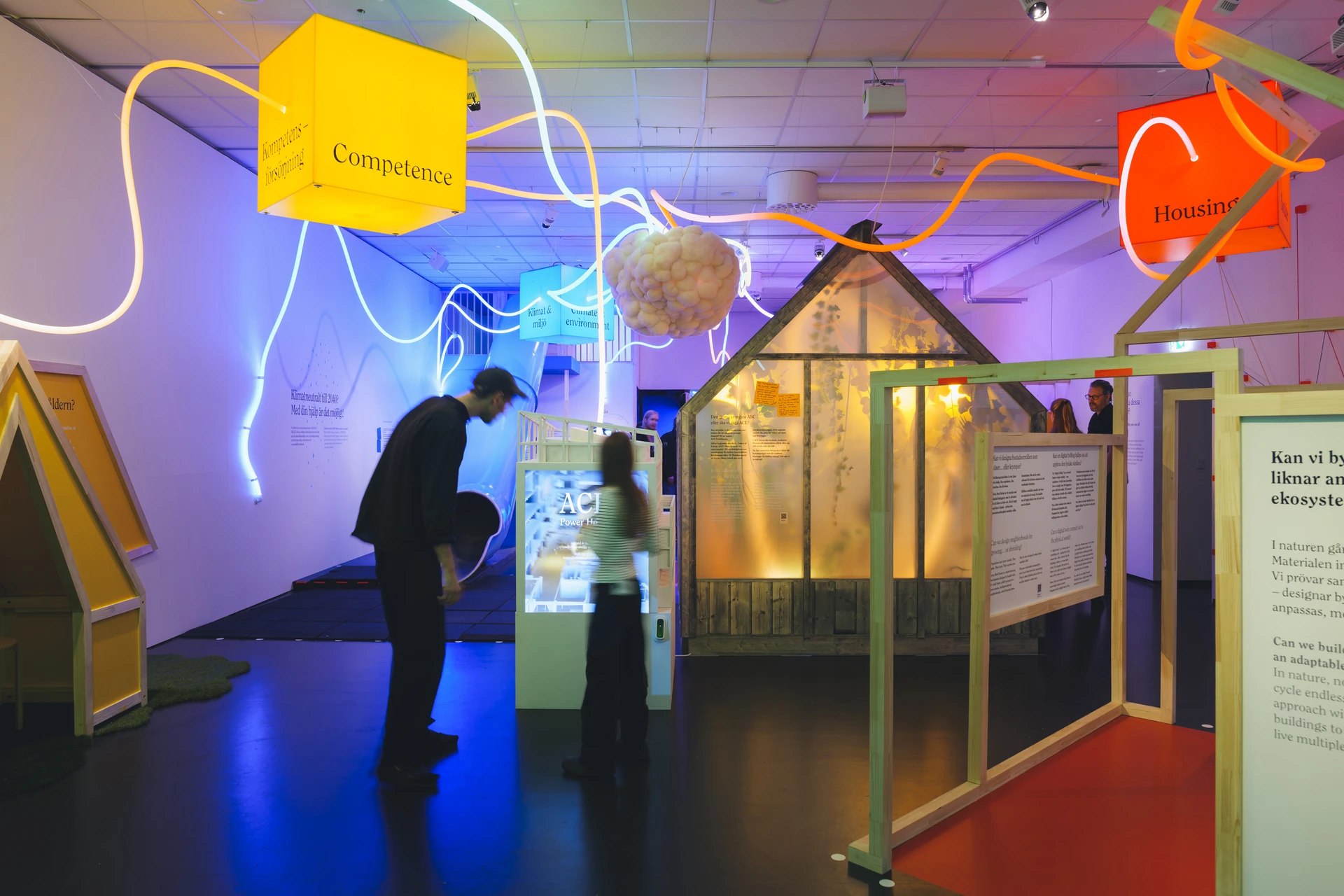 Visitors stand beside the warmly lit greenhouse, with the cloud and looping light lines overhead.