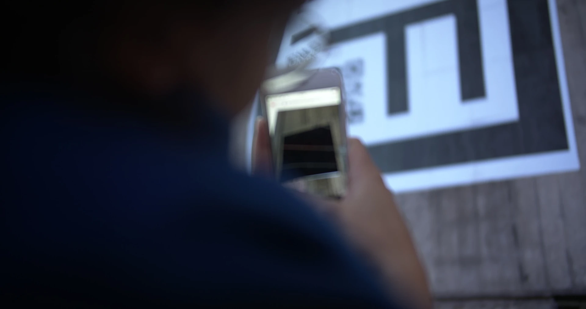 Seen over a shoulder, a phone held up to the marker on the pillar shows the marker on its screen.
