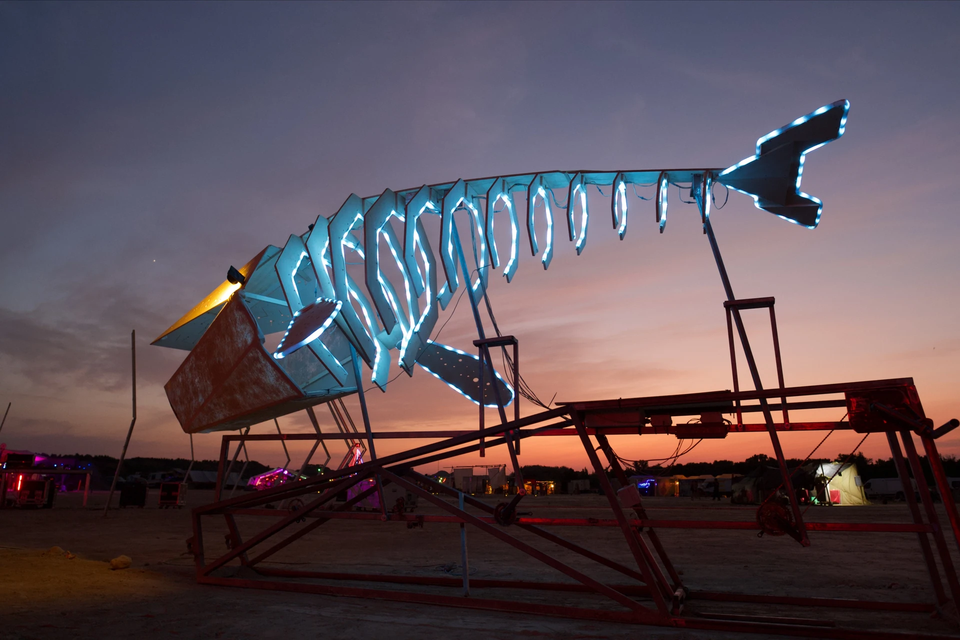 A low side view of the whale with cyan ribs and a raised tail against the evening sky, its metal mechanism visible underneath.
