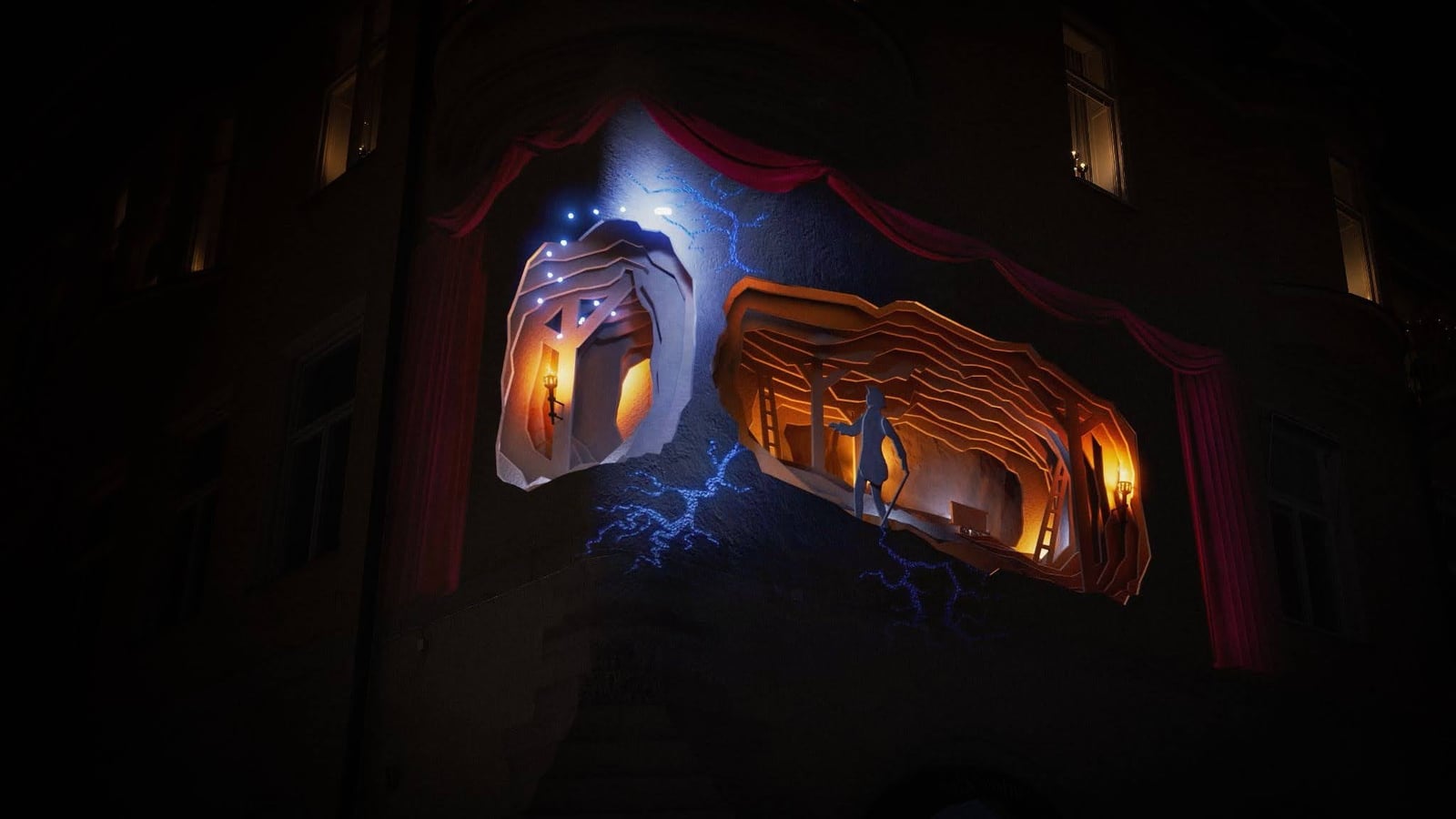 An illuminated face and warm architectural forms are projected across a curved building facade at night.