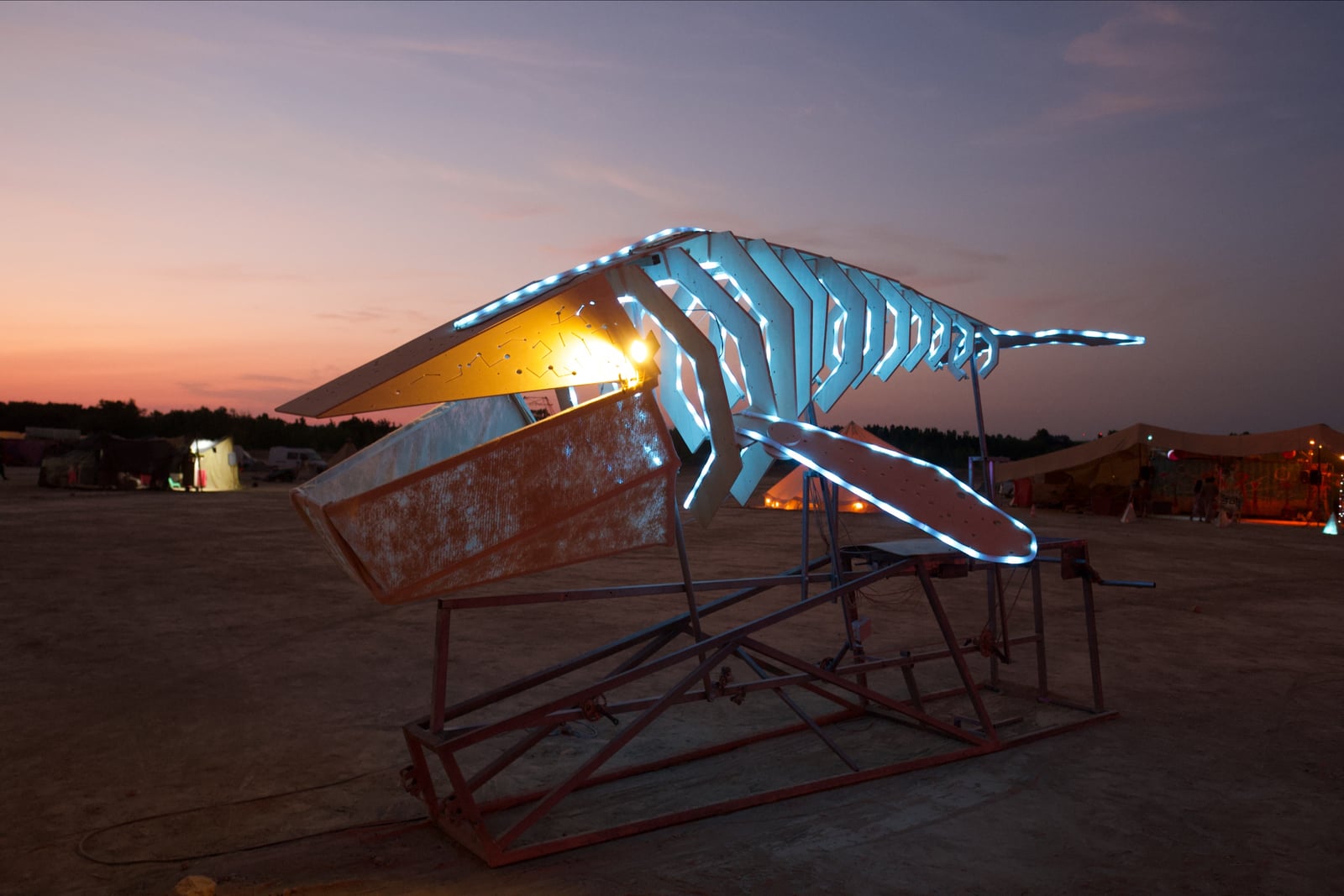 Balena Voladora at dusk, with cyan light tracing its ribs, fins and tail and a warm yellow light beside its open mouth.
