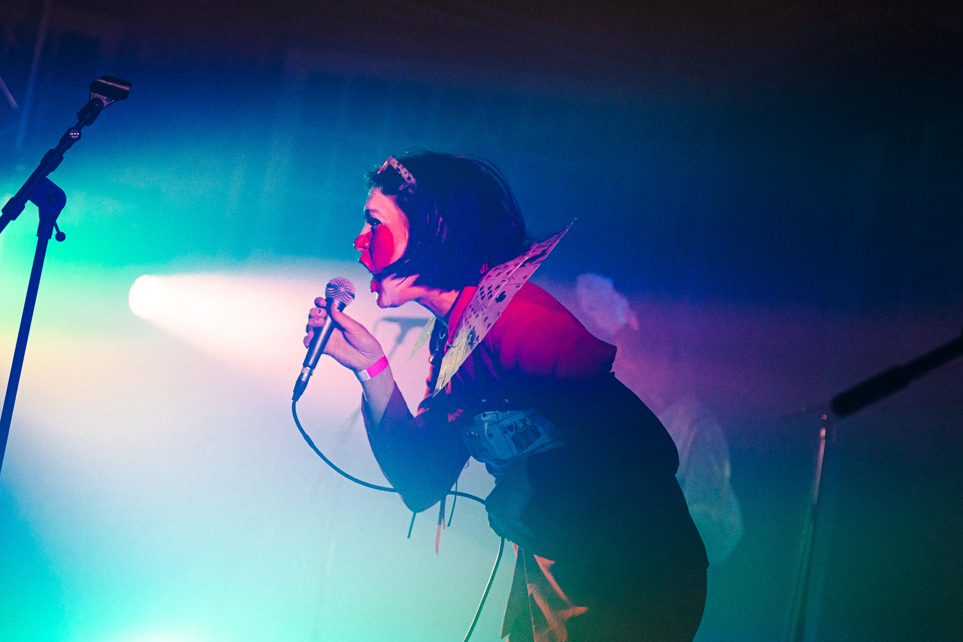 A singer leans into the microphone, lit from the side in cyan and magenta that bleeds across the frame.