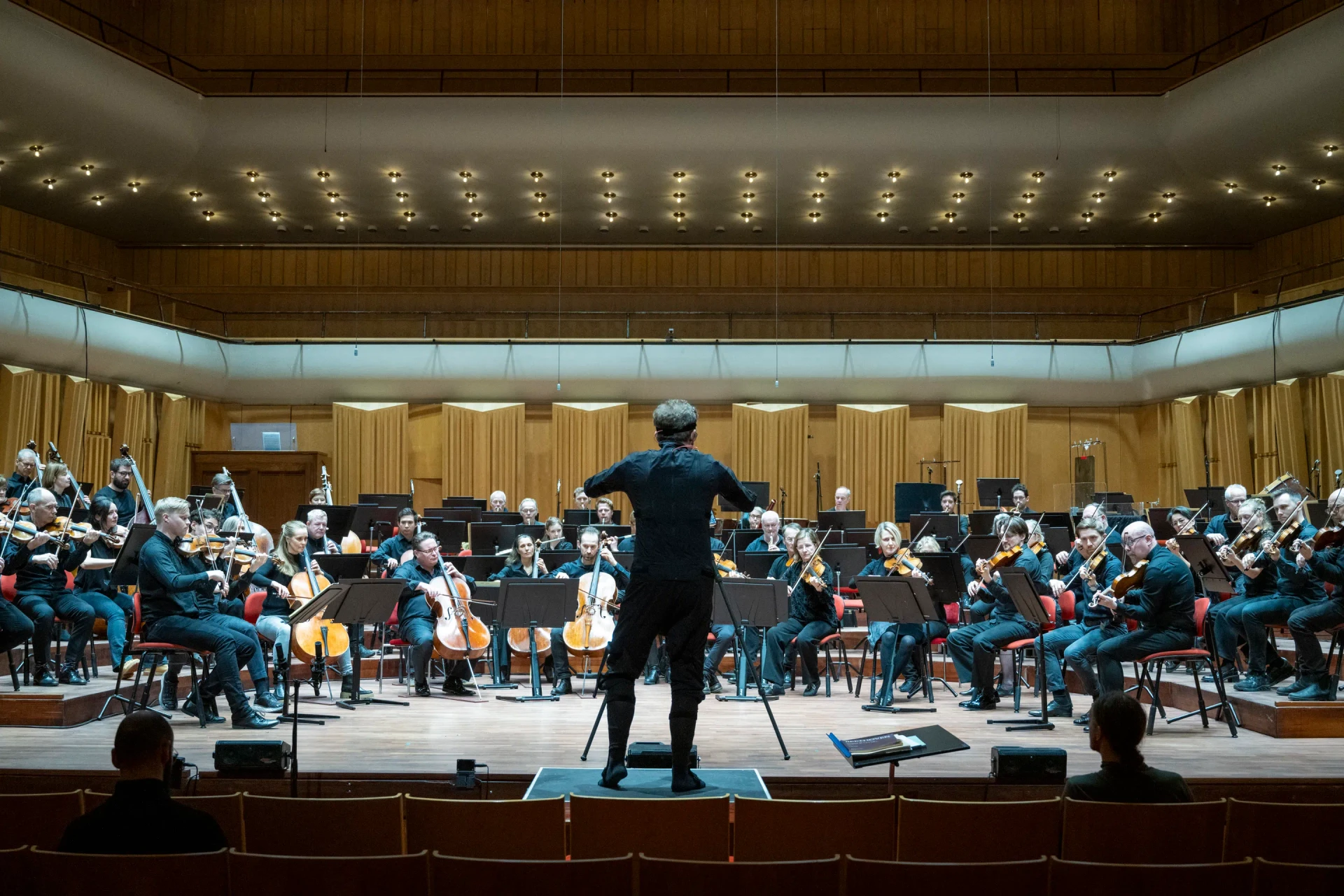 The orchestra gathers around a conductor during a recording session in the concert hall.