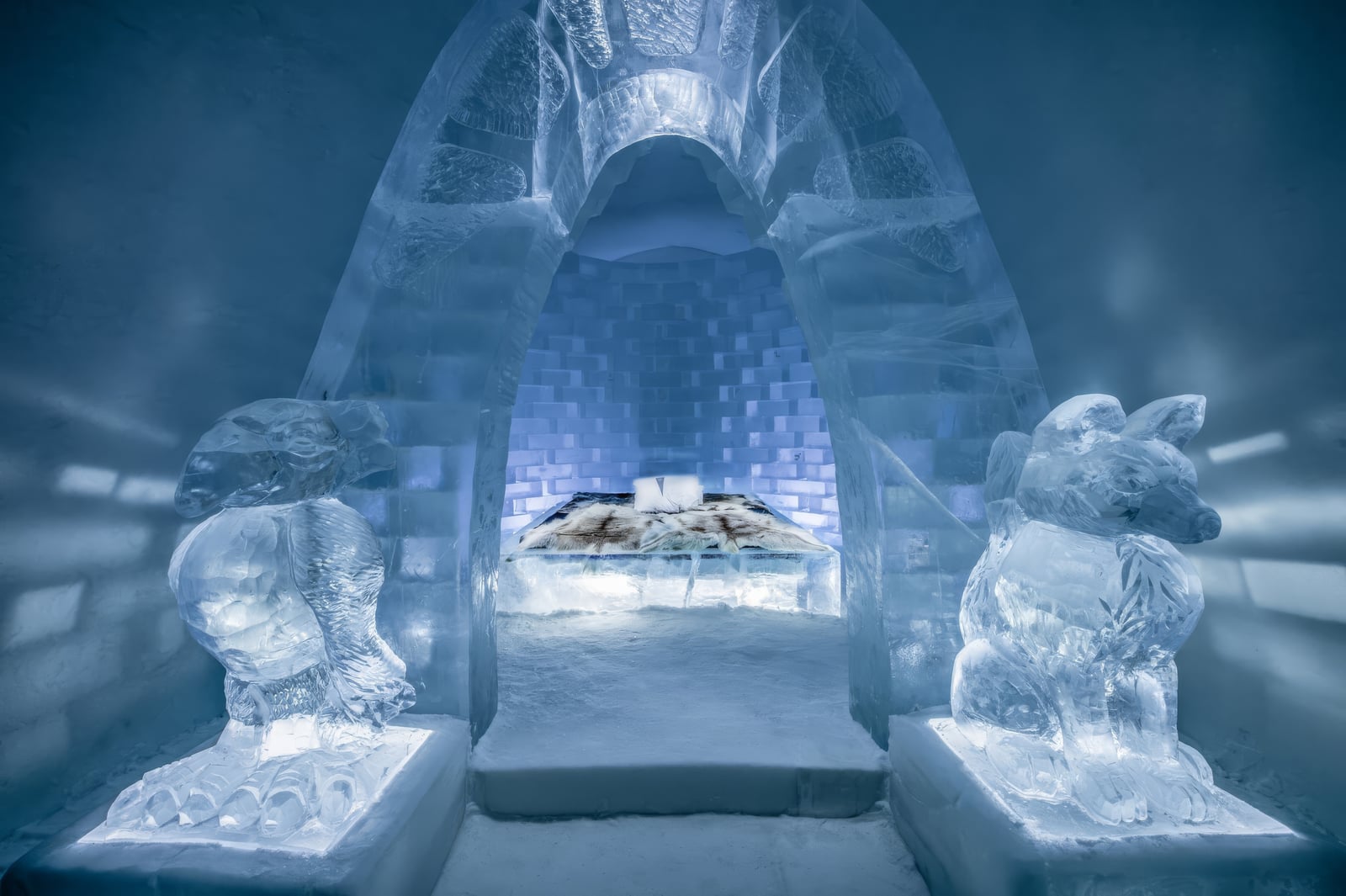 An ice bed sits within a tall carved alcove, flanked by ice sculptures and lit in pale blue.
