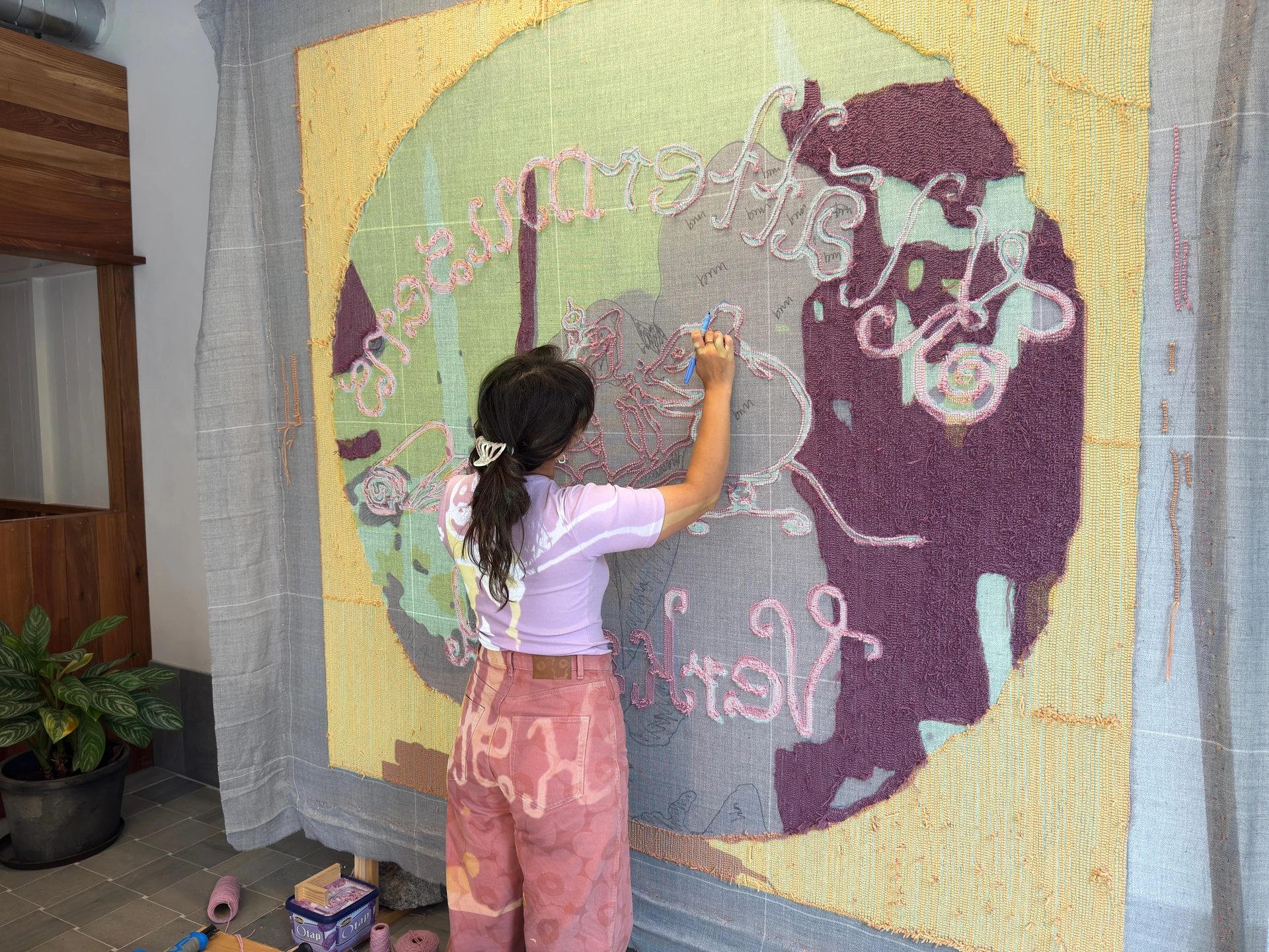 Rose marks the sewing-mouse outline on the back of the partly tufted rug, with pink, plum and yellow yarn surrounding the unfinished cloth.