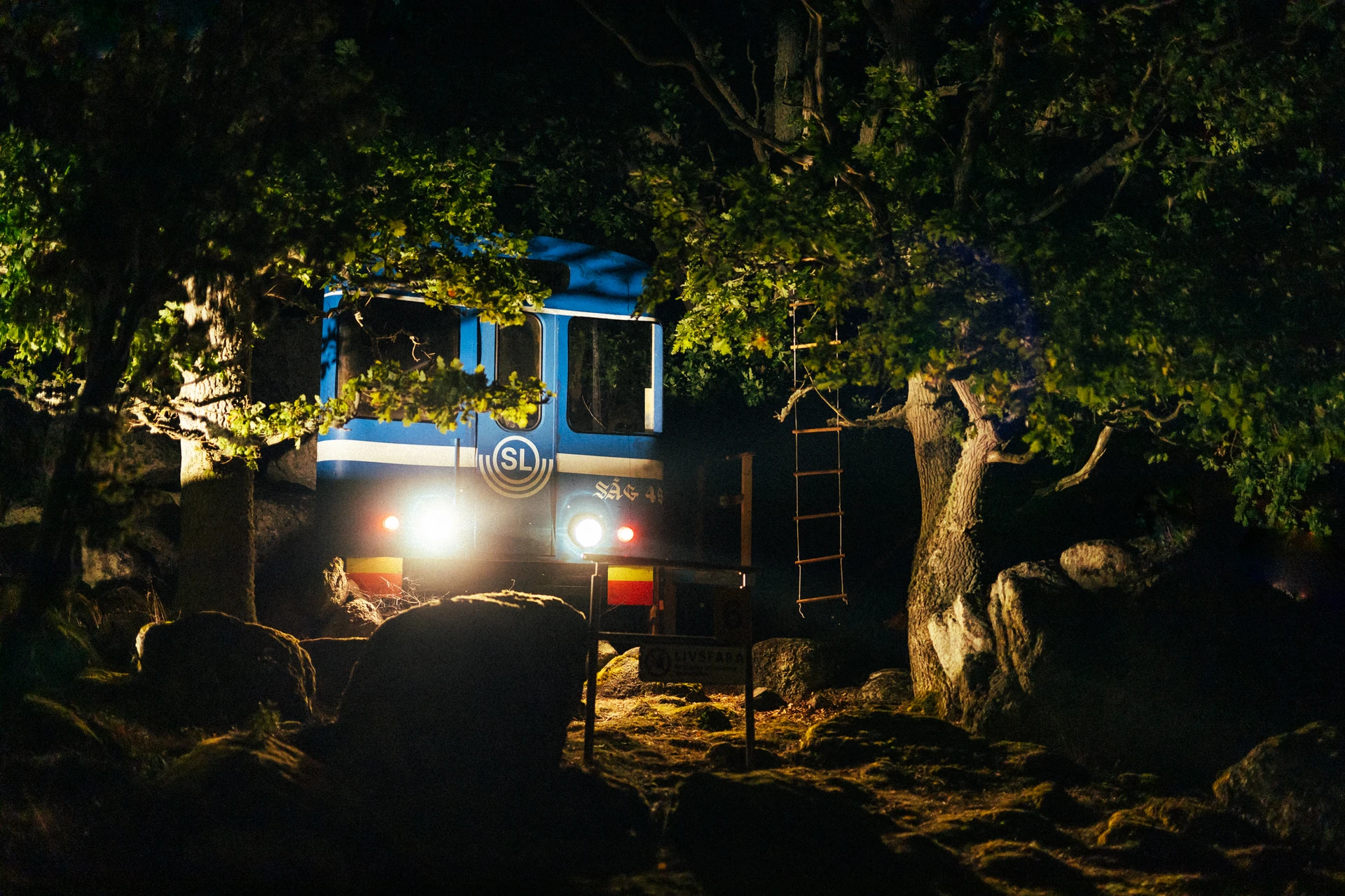 A truck parked among trees at night, its headlights and a blue-lit cabin glowing through the branches.