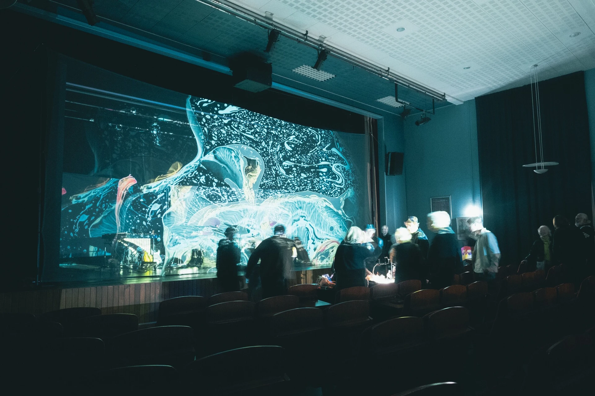 After the concert, the audience gathers at the front of the hall under a large projection of marbled colour.