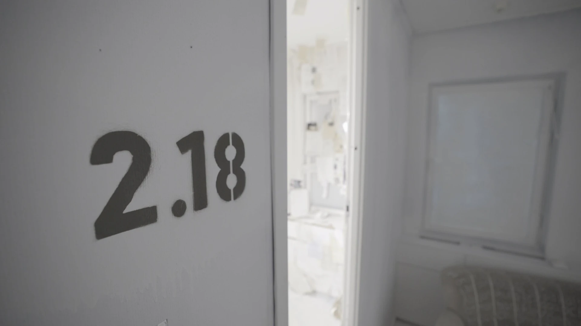 The room number 2.18 stencilled in black on a white wall beside an open door.
