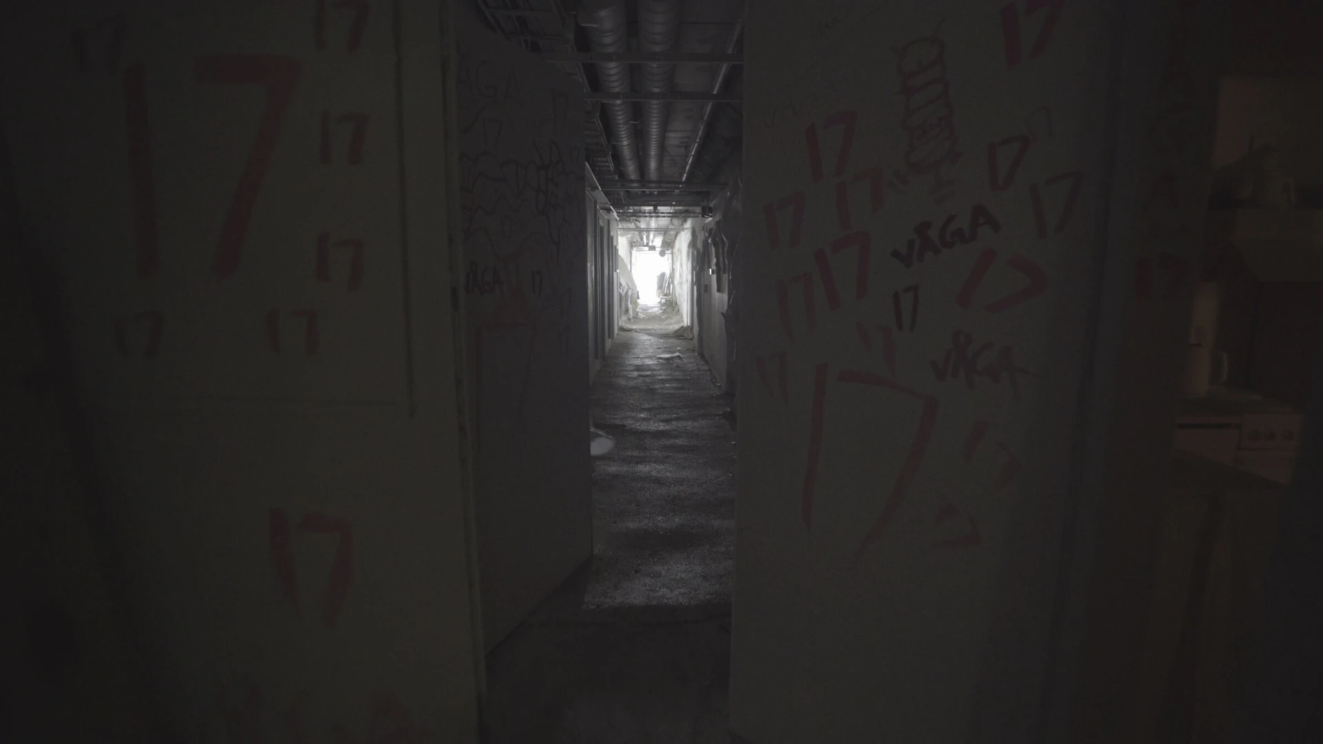 A long, dim corridor with red numbers painted on the walls and a bright light at the far end.