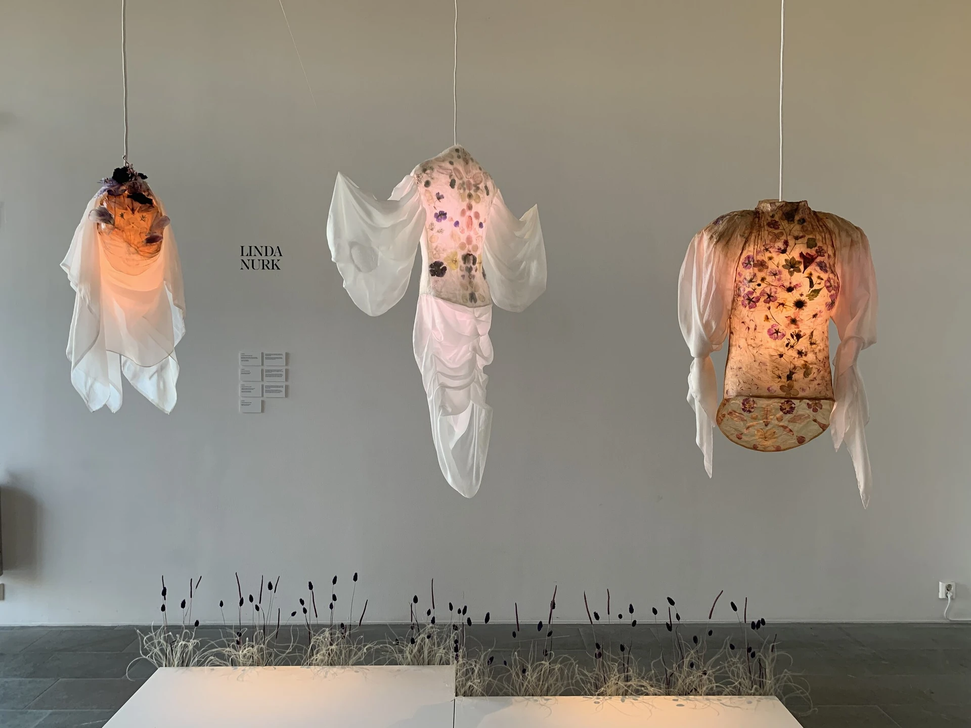 Three of Linda Nurk's lit textile sculptures hang above a bed of dried grasses at Sven-Harrys konstmuseum.