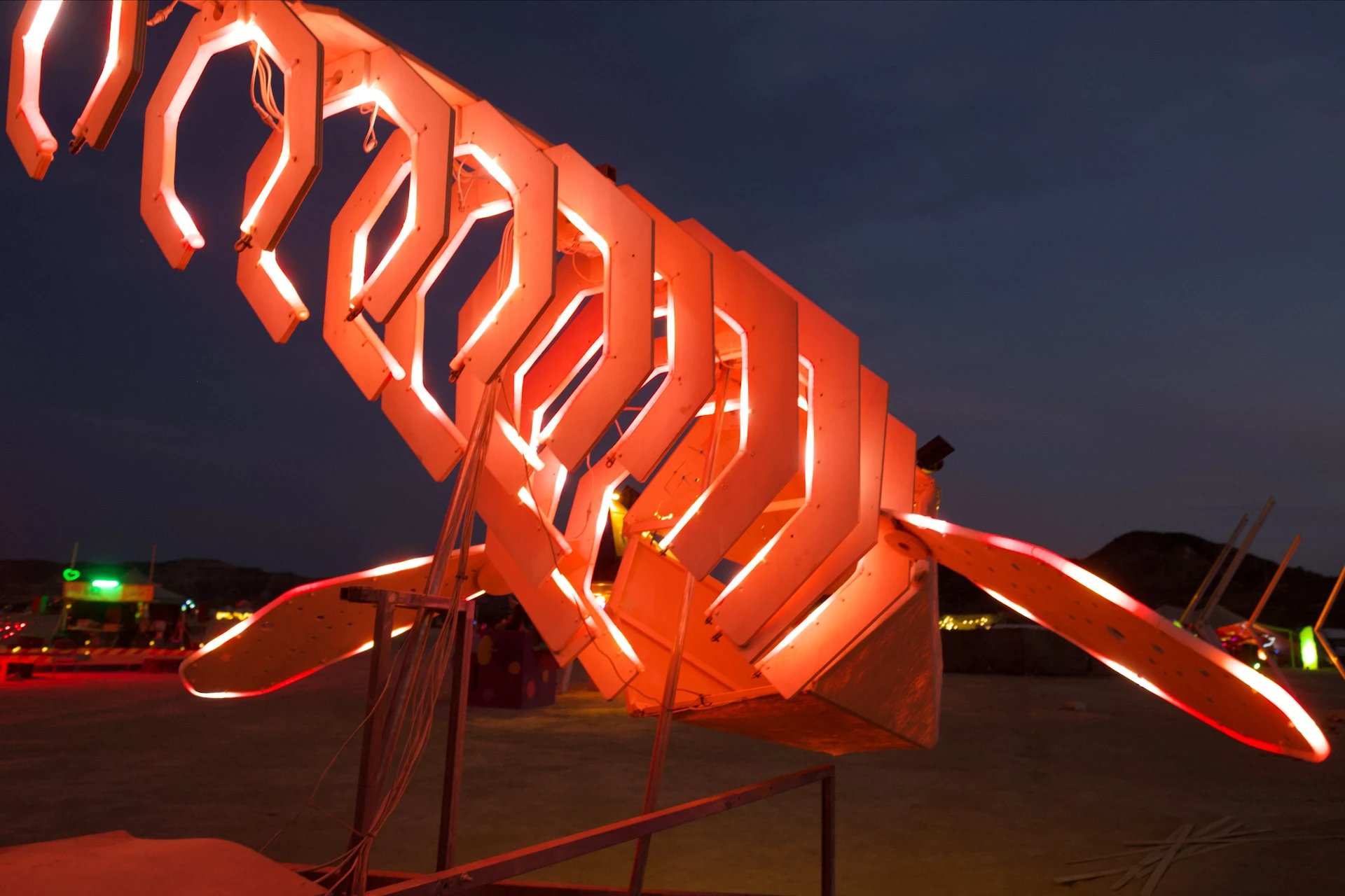 A close view along the illuminated ribs towards the whale's head, showing red LED tubes, cables and the spread fins.