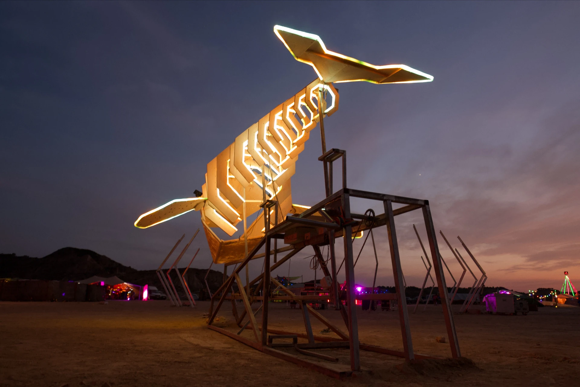 The whale seen from beneath its tail, with warm light outlining the ribs and both fins against a blue dusk sky.