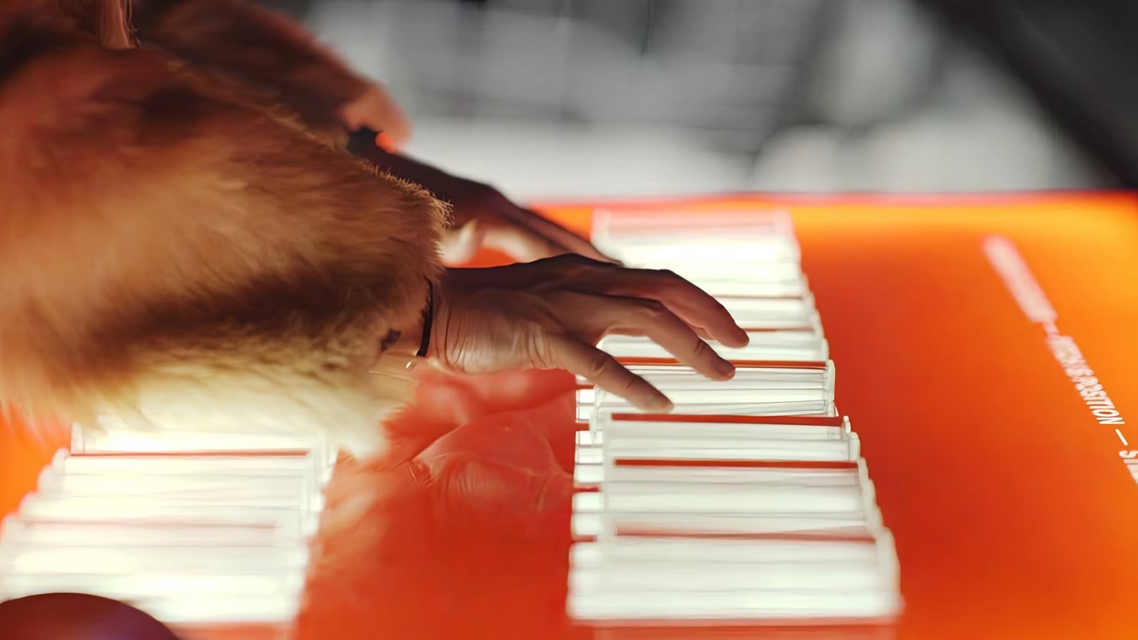 Hands play a small illuminated keyboard on an orange tabletop, the public controller for Harpa’s facade.