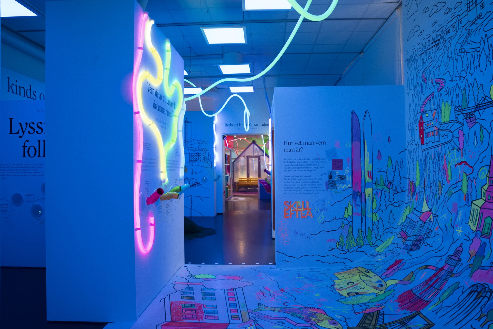 Blue light fills a passage between a listening wall and a hand-coloured mural, with luminous lines continuing across the ceiling.