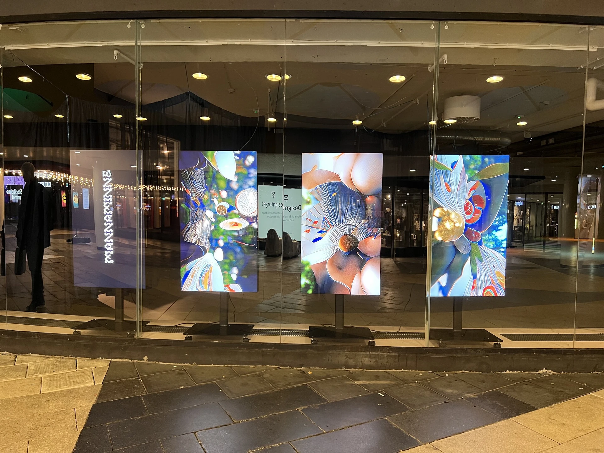 From the passage outside, three hanging scrims glow behind the glass front of Superellipsen, beside a sign with the title in vertical letters.