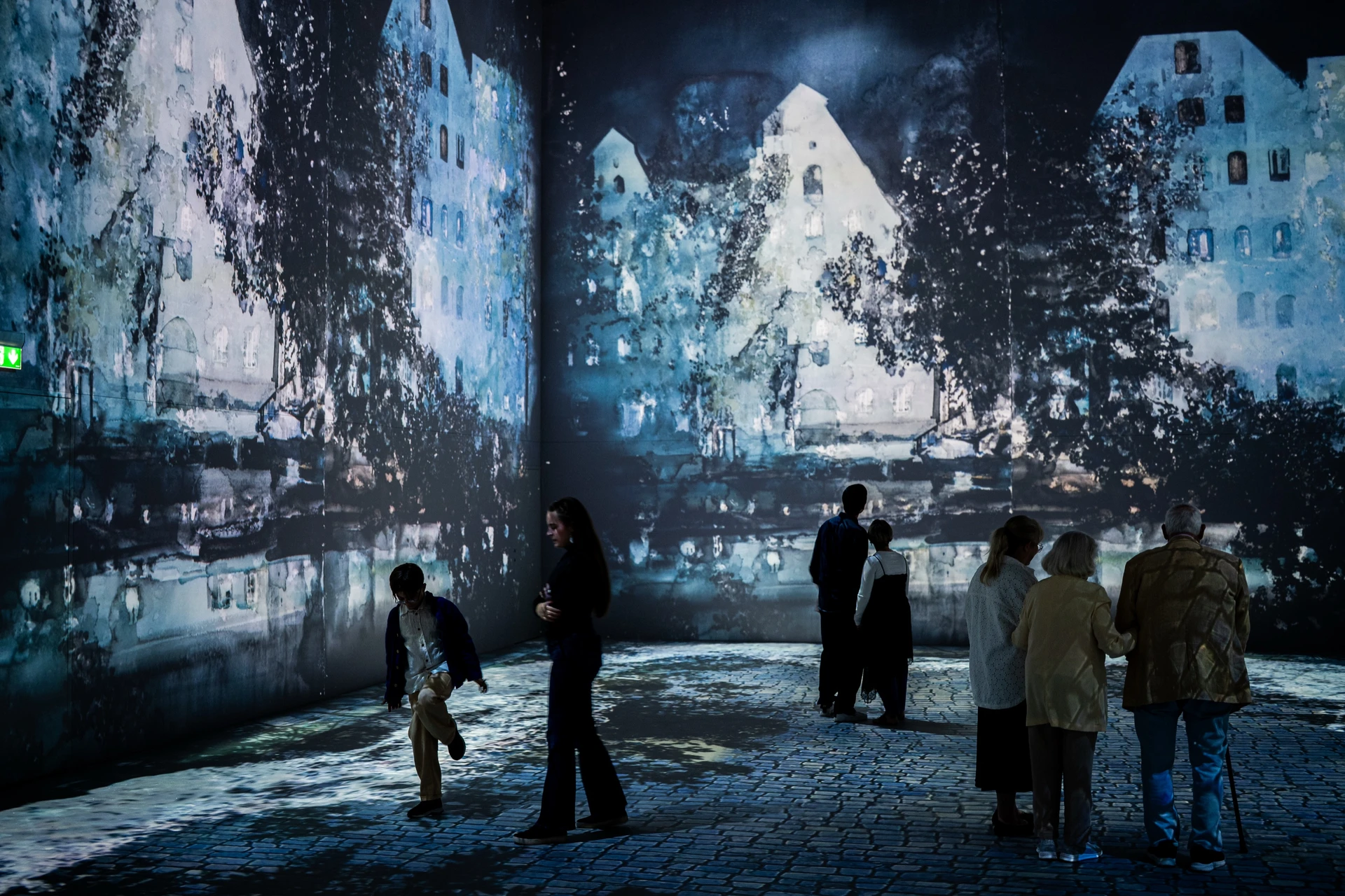 Visitors walk across a cobbled floor projection beneath Lars Lerin's blue night watercolours of tall houses and trees.