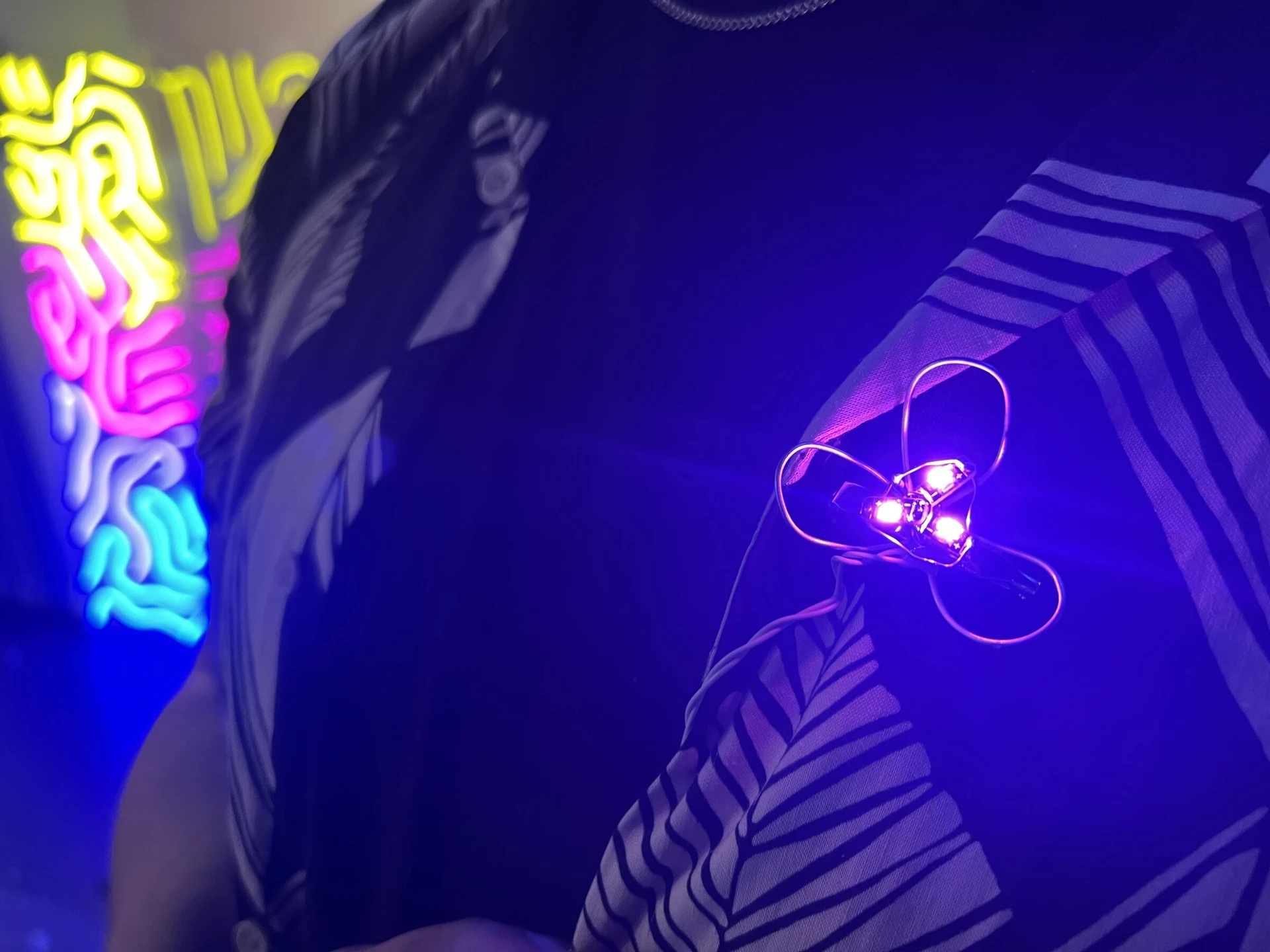 A small LED sequin glows violet on a workshop participant's shirt, the neon-like signs behind.