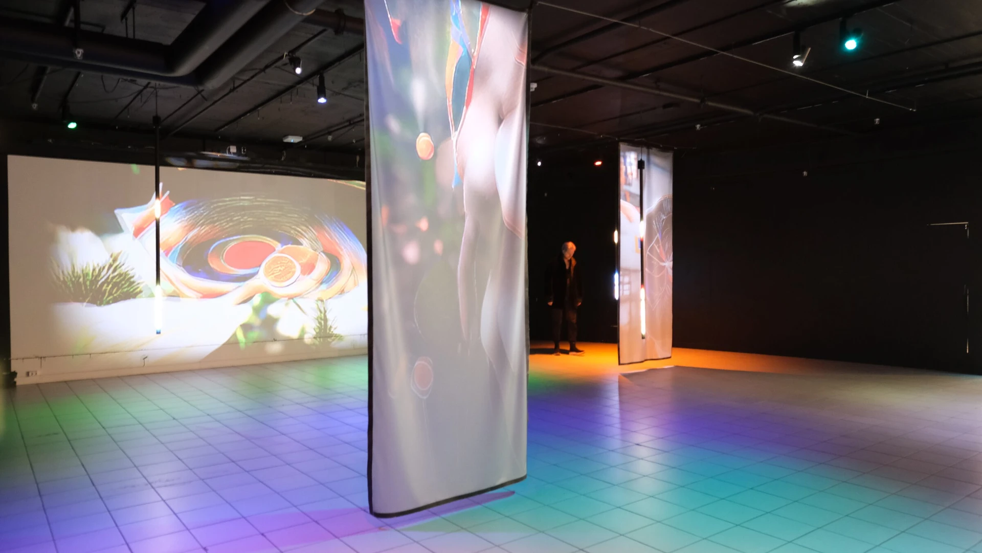The room from another angle: the wall projection, a lit scrim and coloured light across the floor, with figures at the far end.