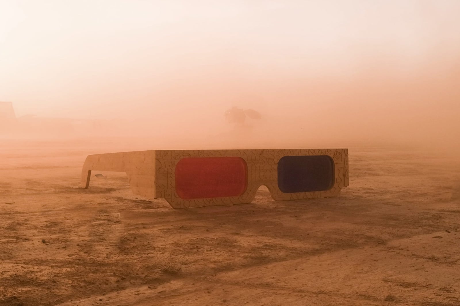 An oversized pair of red-and-blue 3D glasses rests on a dusty plain in warm evening light.