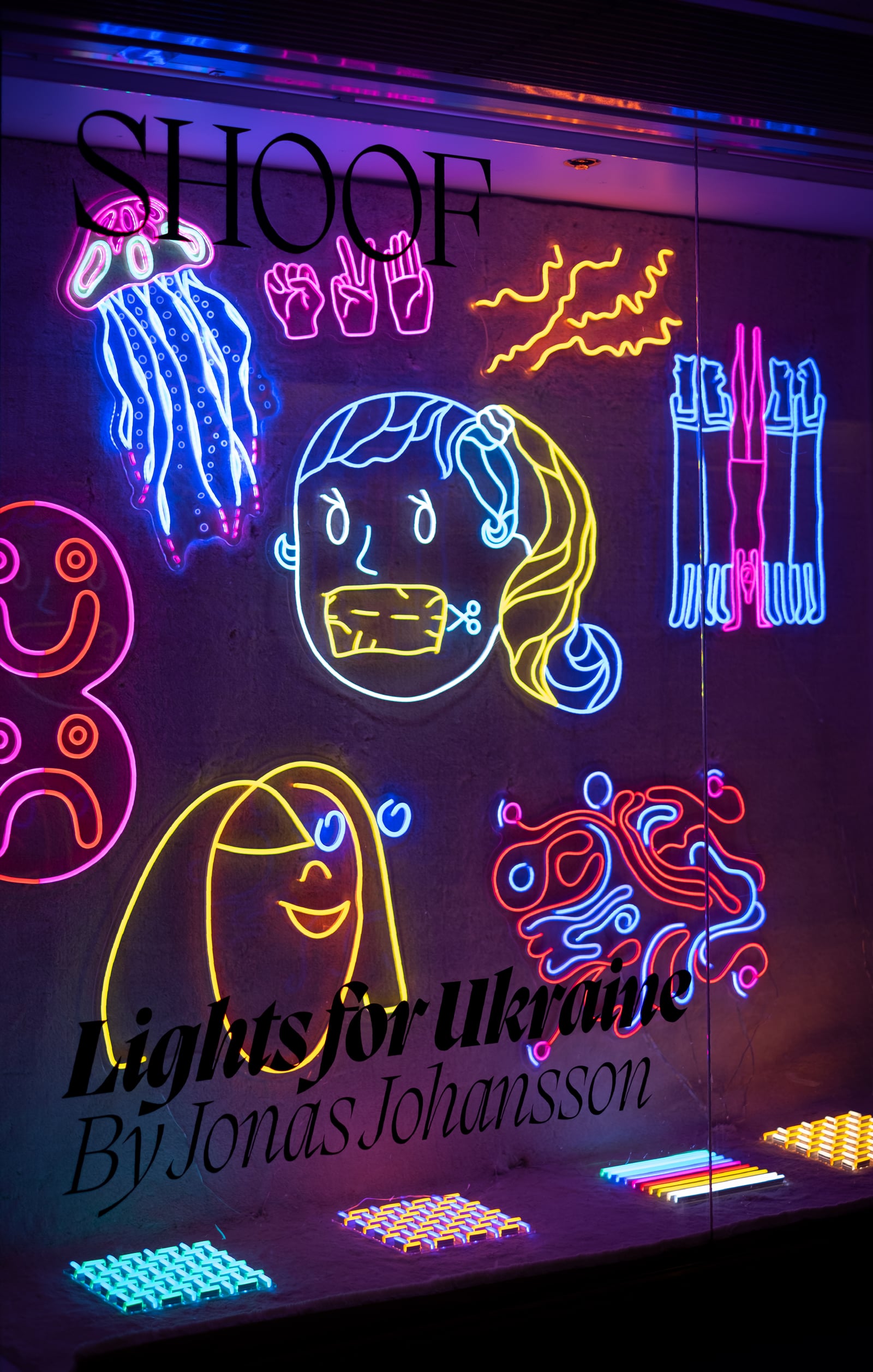 Colourful illuminated drawings of hands, flowers and faces fill a window as LED signs.