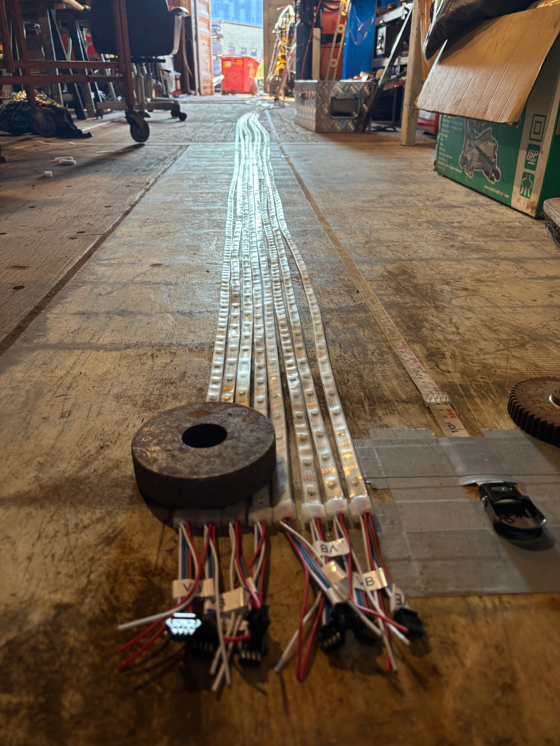 Long LED strips are laid out and illuminated on a workshop floor, with wiring gathered at their ends.