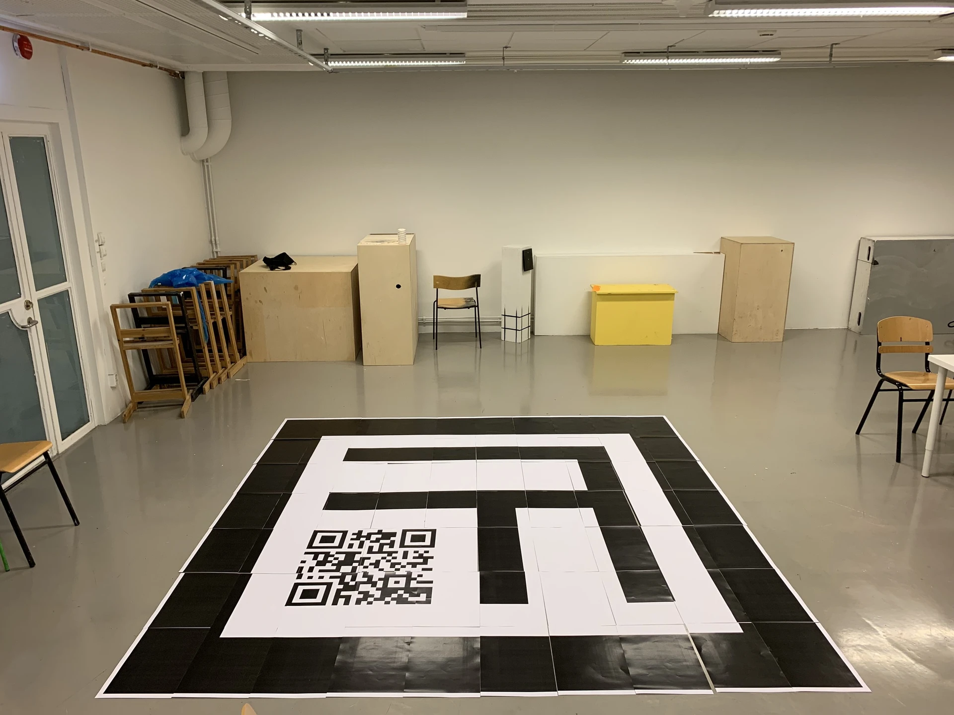 The marker laid out on the floor of an empty classroom, its black frame, stripes and QR code assembled from many printed sheets.