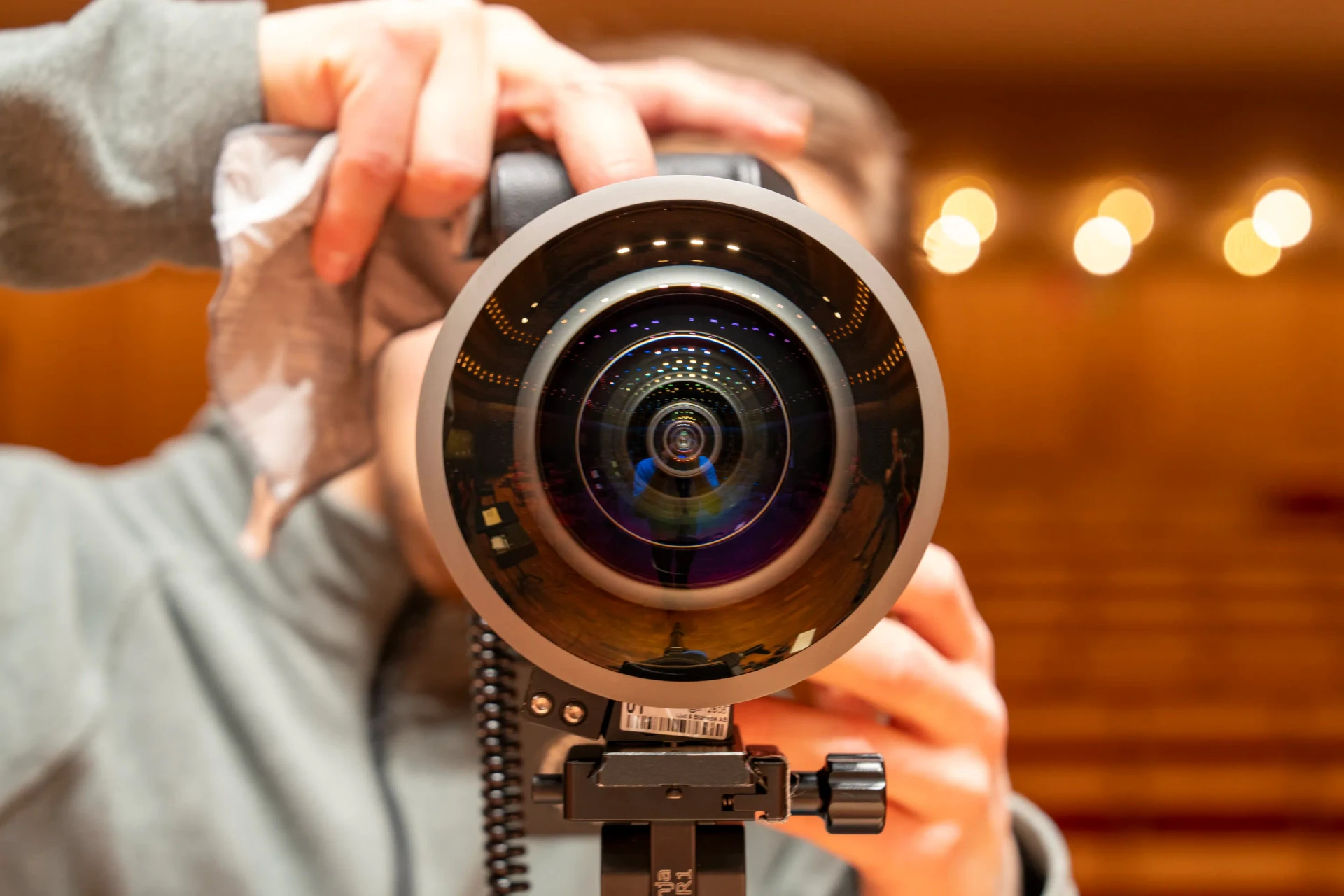 A close view of the fisheye camera lens, with the concert hall reflected in its glass.