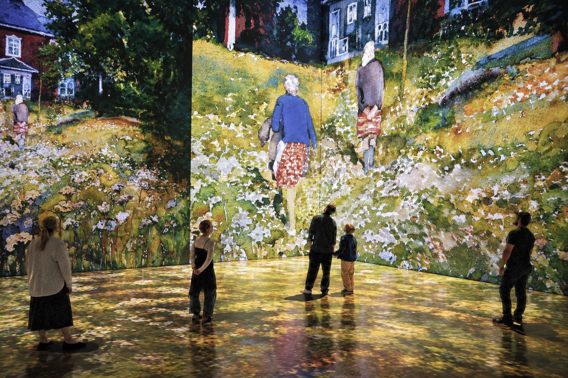 Visitors stand inside a projected summer meadow of wildflowers, with painted figures walking across the walls.