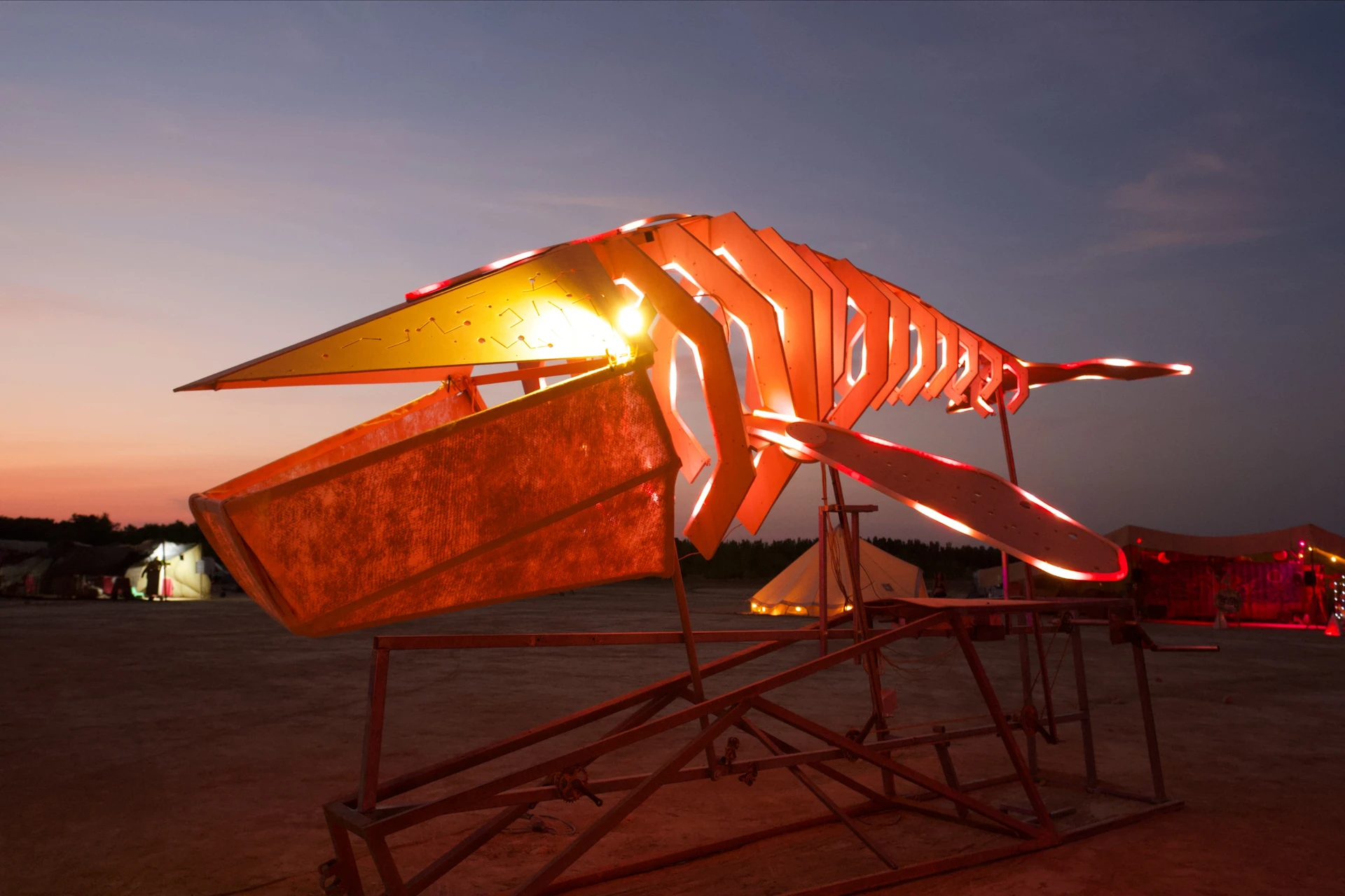 The whale's open mouth, ribs and near fin glow orange and red against a pink evening sky.
