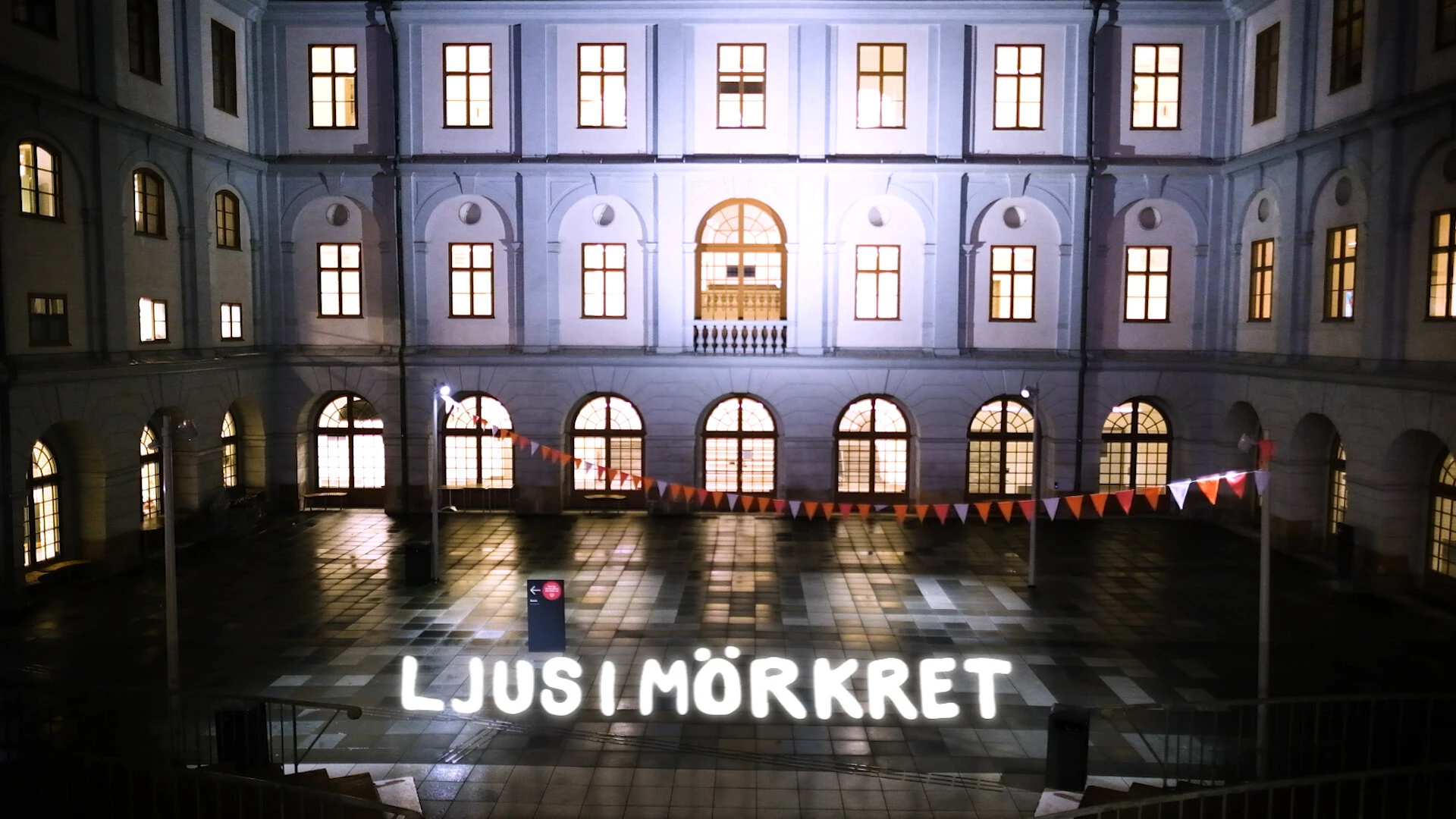 Ljus i mörkret in light letters across the rain-wet courtyard of Stadsmuseet, its windows lit.