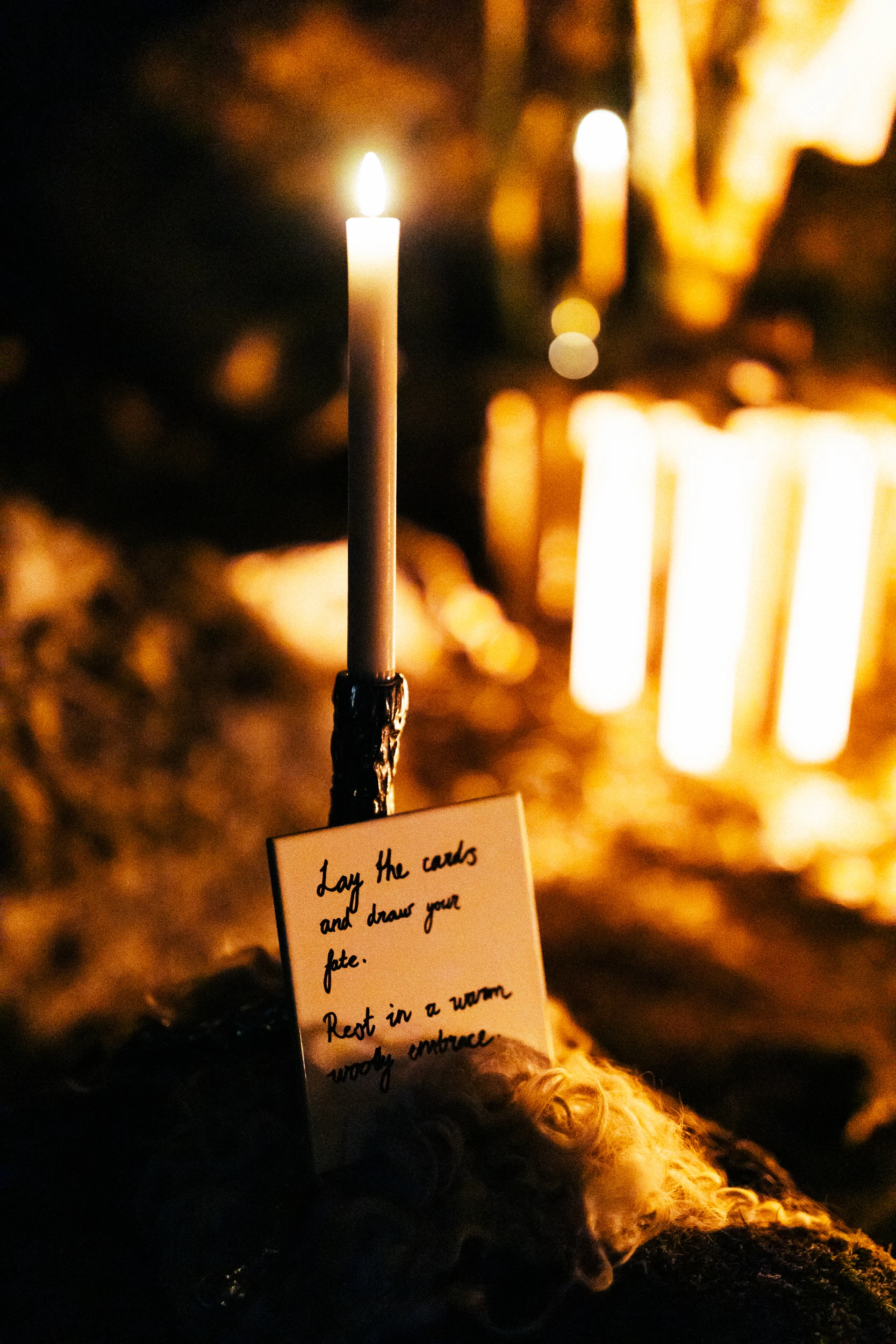 A tall candle burns on the rock beside a handwritten note, with more candles glowing behind it.