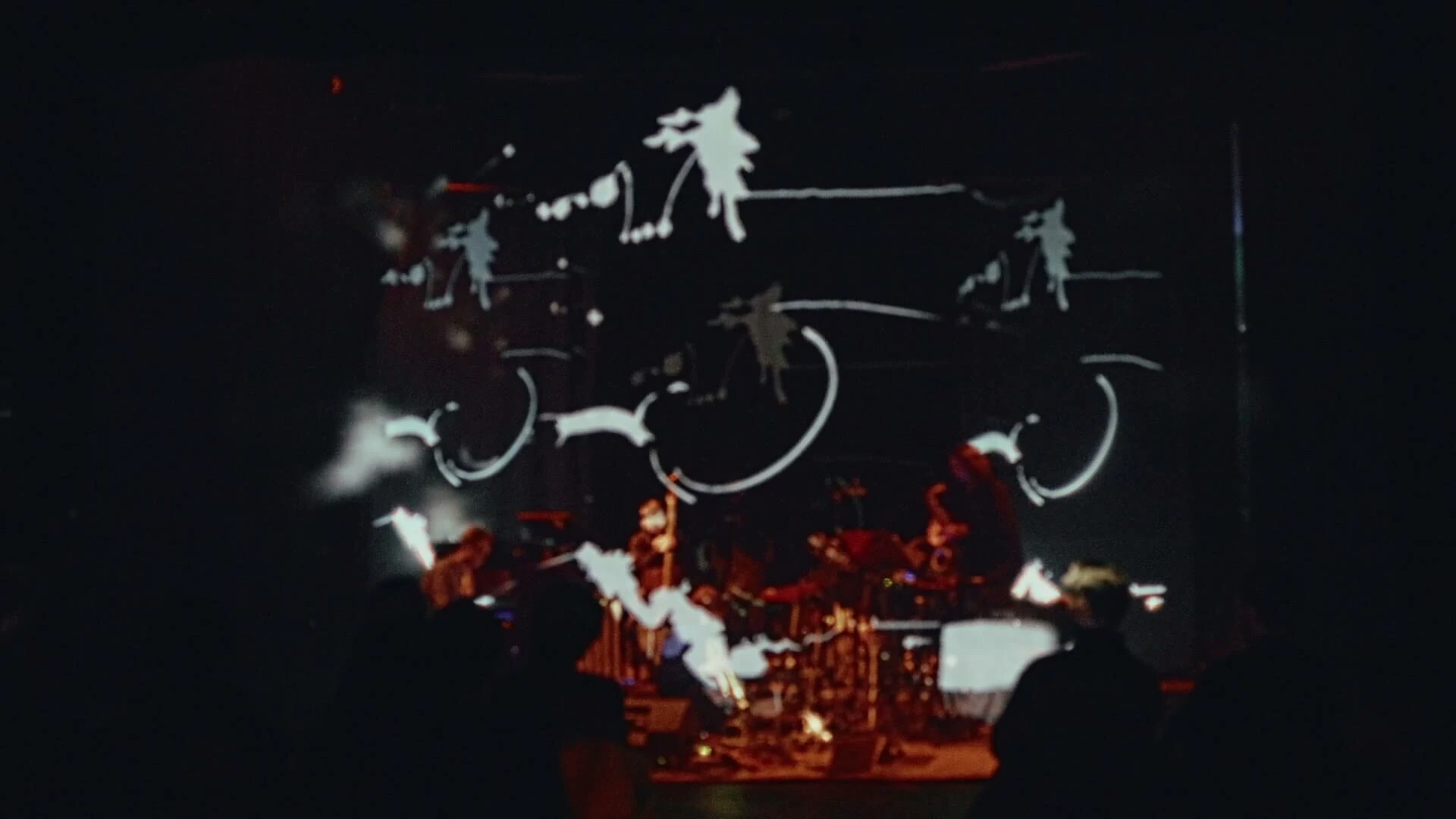 Curved white marks and dots of a live-drawn score hang above the musicians in the dark.