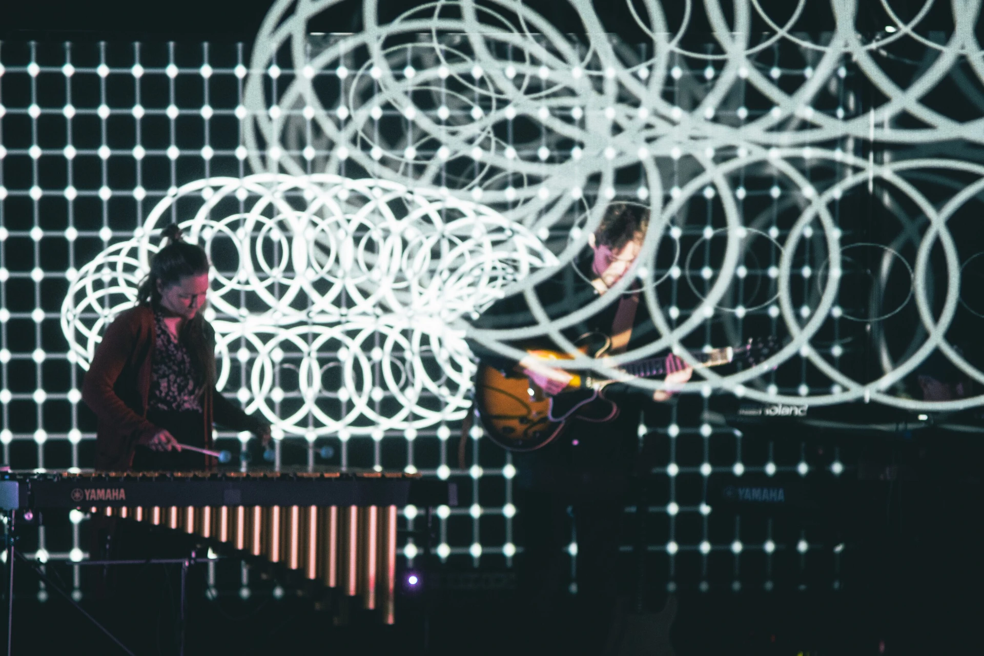 The vibraphonist and guitarist play inside a projected field of white rings and a grid of dots.