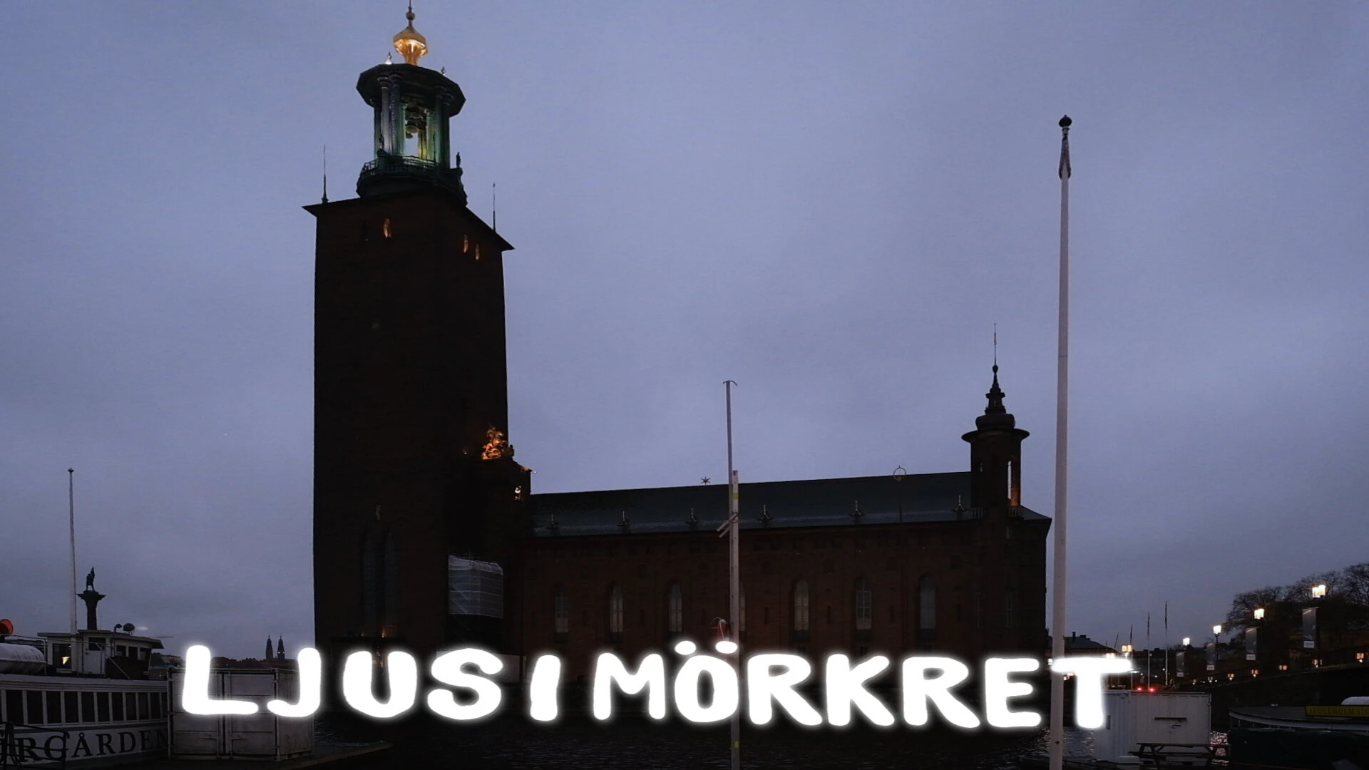 Ljus i mörkret in rounded light letters on the quay in front of Stockholm City Hall at dusk.