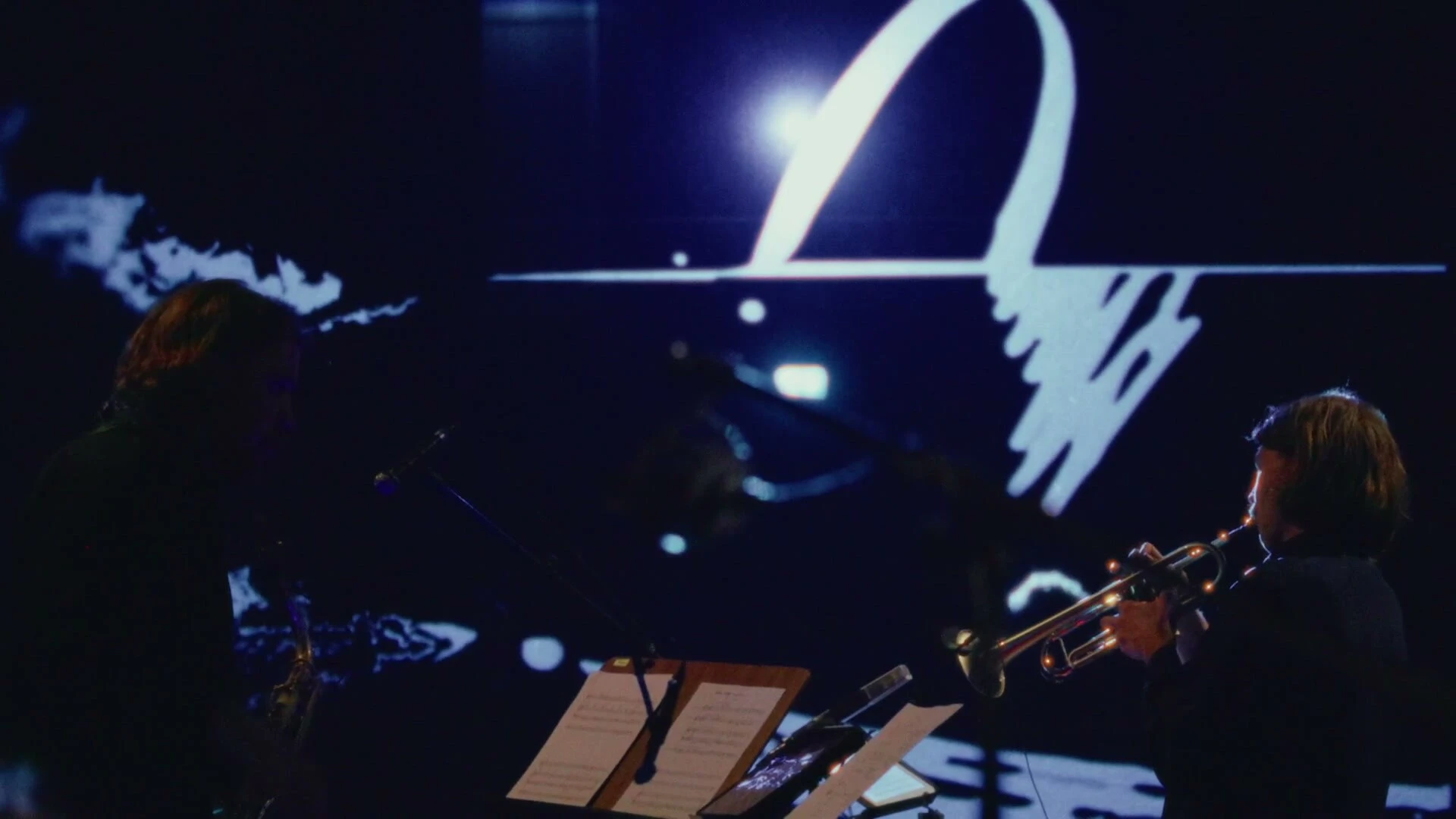 Two of the musicians in profile at Barnens Scen, with bold white strokes of a live-drawn score projected large behind them.