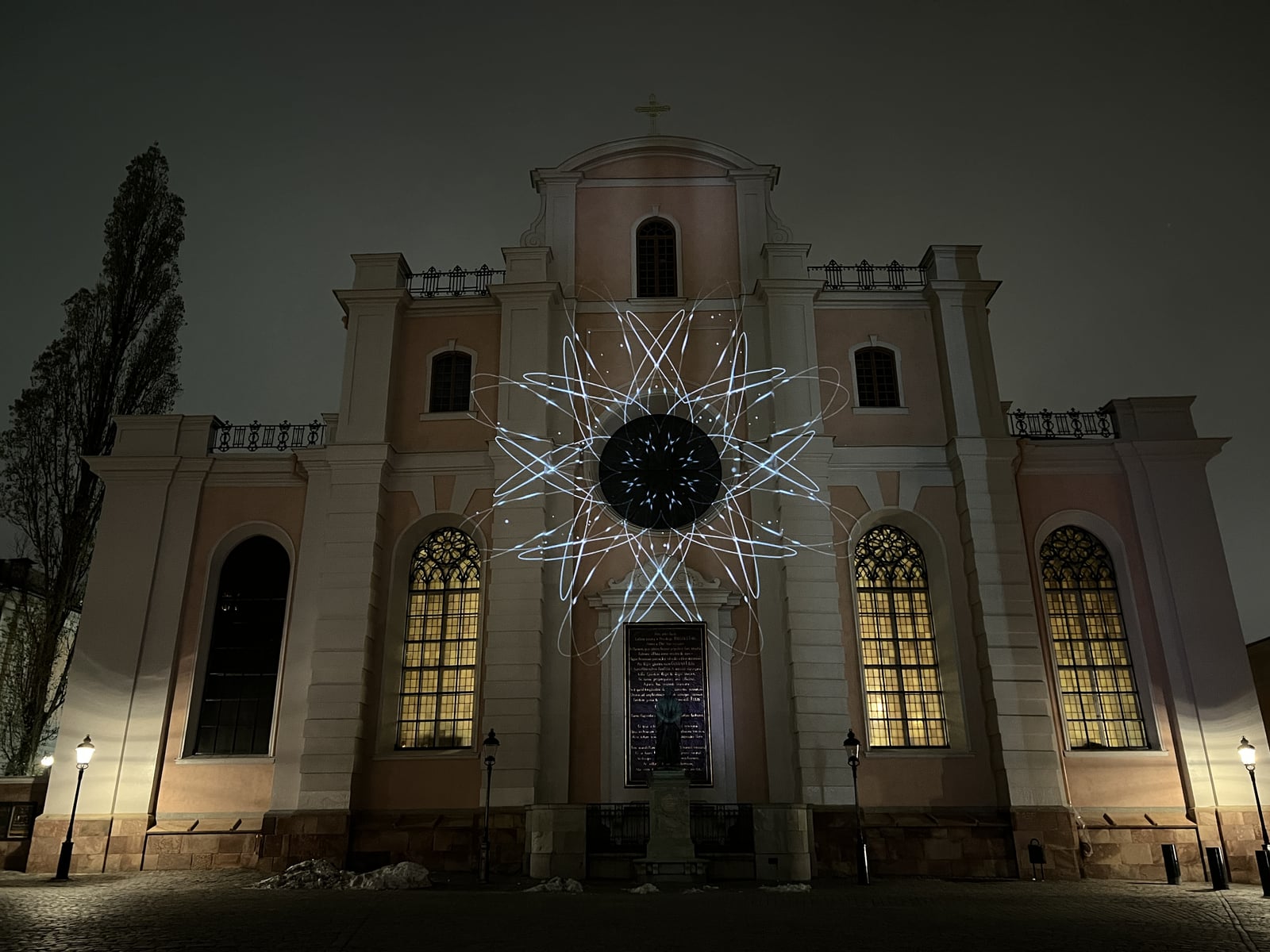 White branching lines radiate from a dark circular centre across the illuminated facade of Storkyrkan at night.
