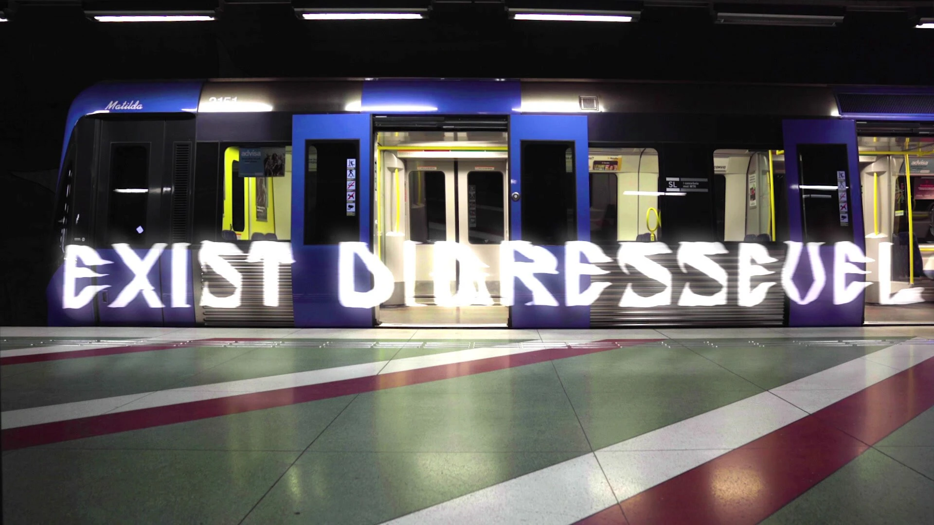 Words in broad light letters, starting with Exist, run along a waiting metro train on a striped platform.