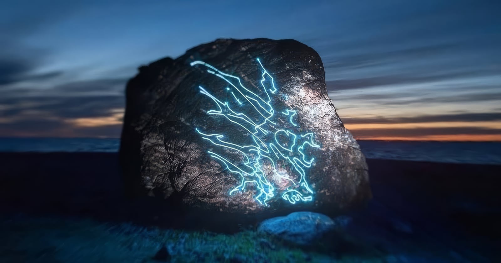 Branching blue-white projections illuminate a large boulder beneath the dusk sky.
