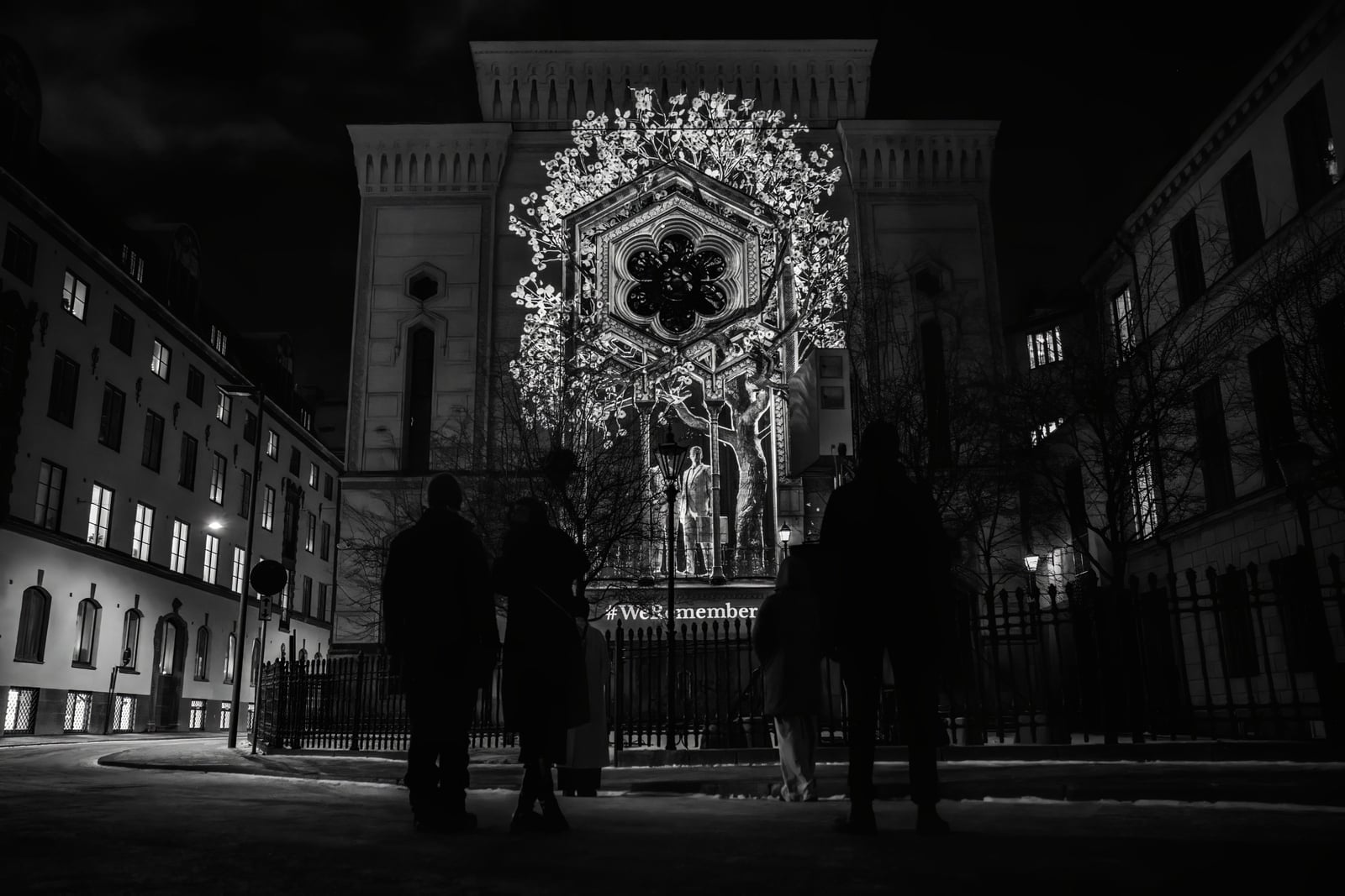 A monochrome projection of sculpted figures covers the Great Synagogue as visitors watch from the street.