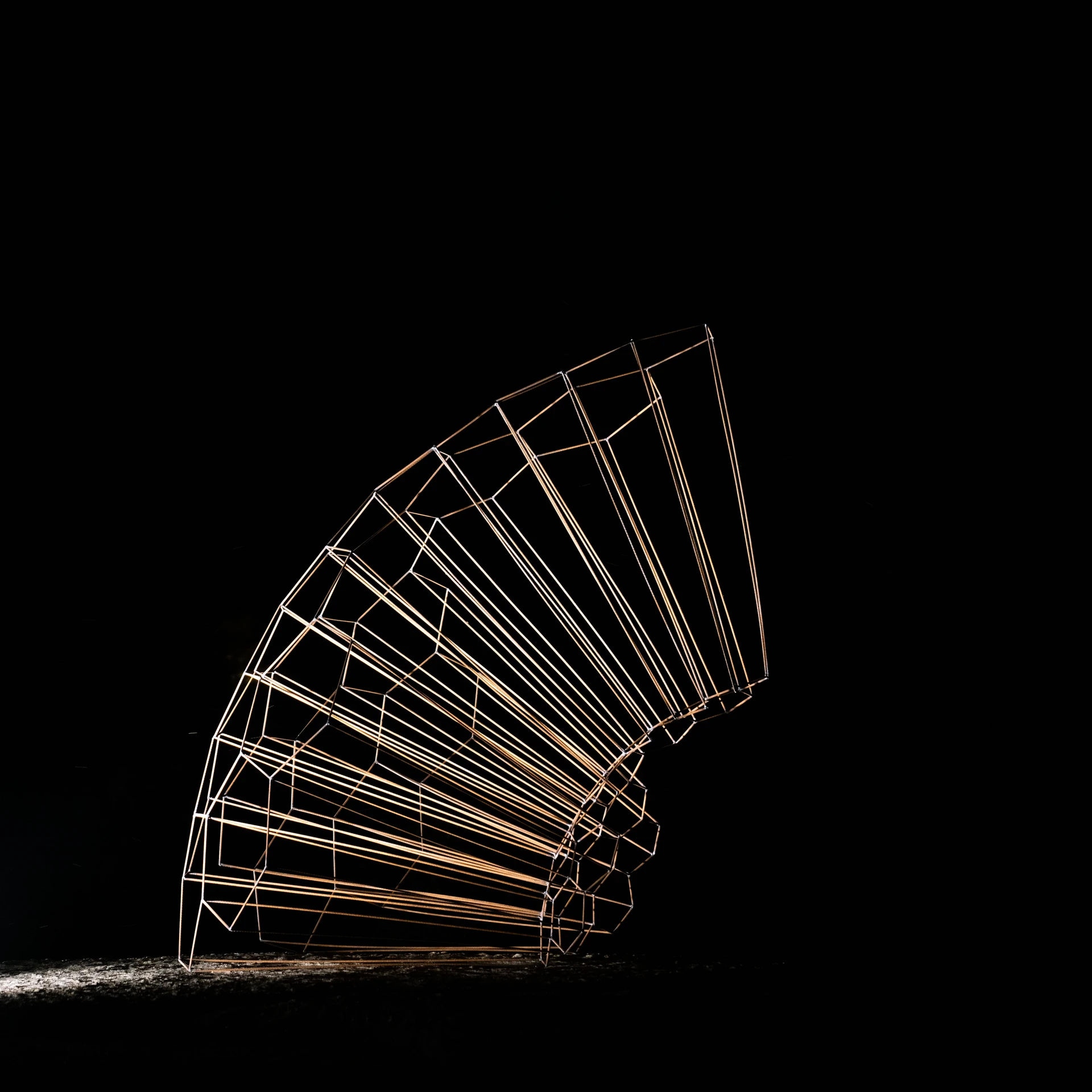 The same steel fan at night, its ribs picked out in white light against complete darkness.