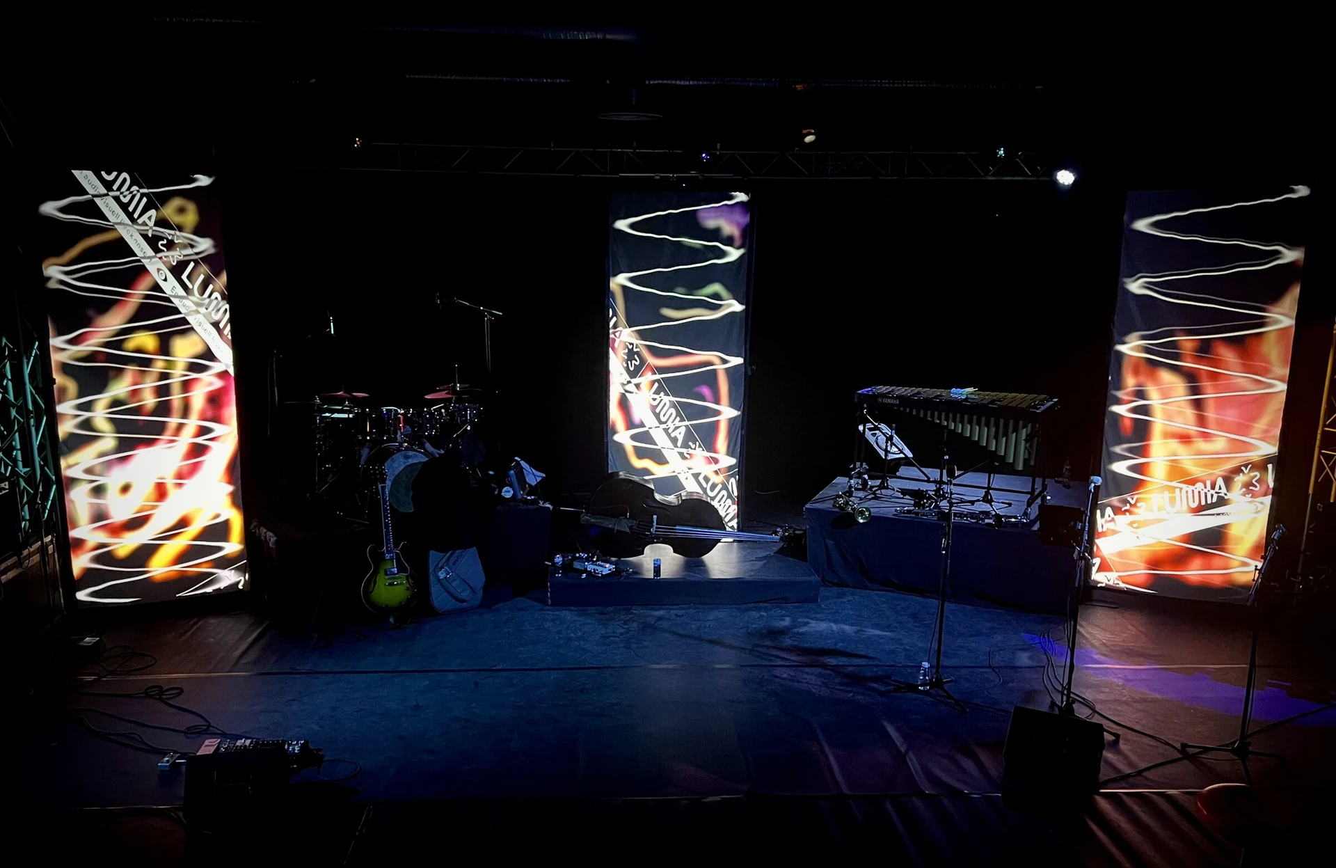 The empty stage before the premiere: drums, double bass and vibraphone between three tall screens showing flame-like shapes, white spirals and the Lumia tape graphic.