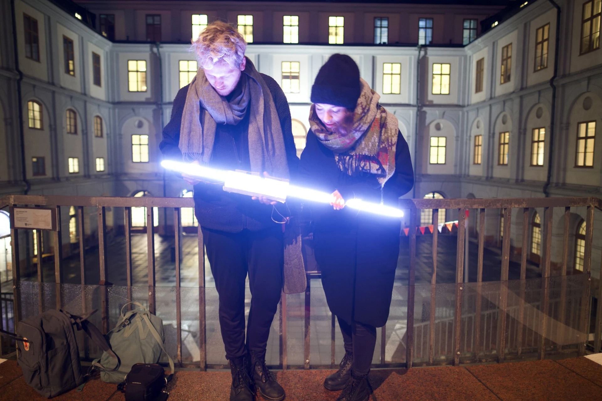 Two people check the lit LED stick on a balcony above the courtyard of Stadsmuseet.