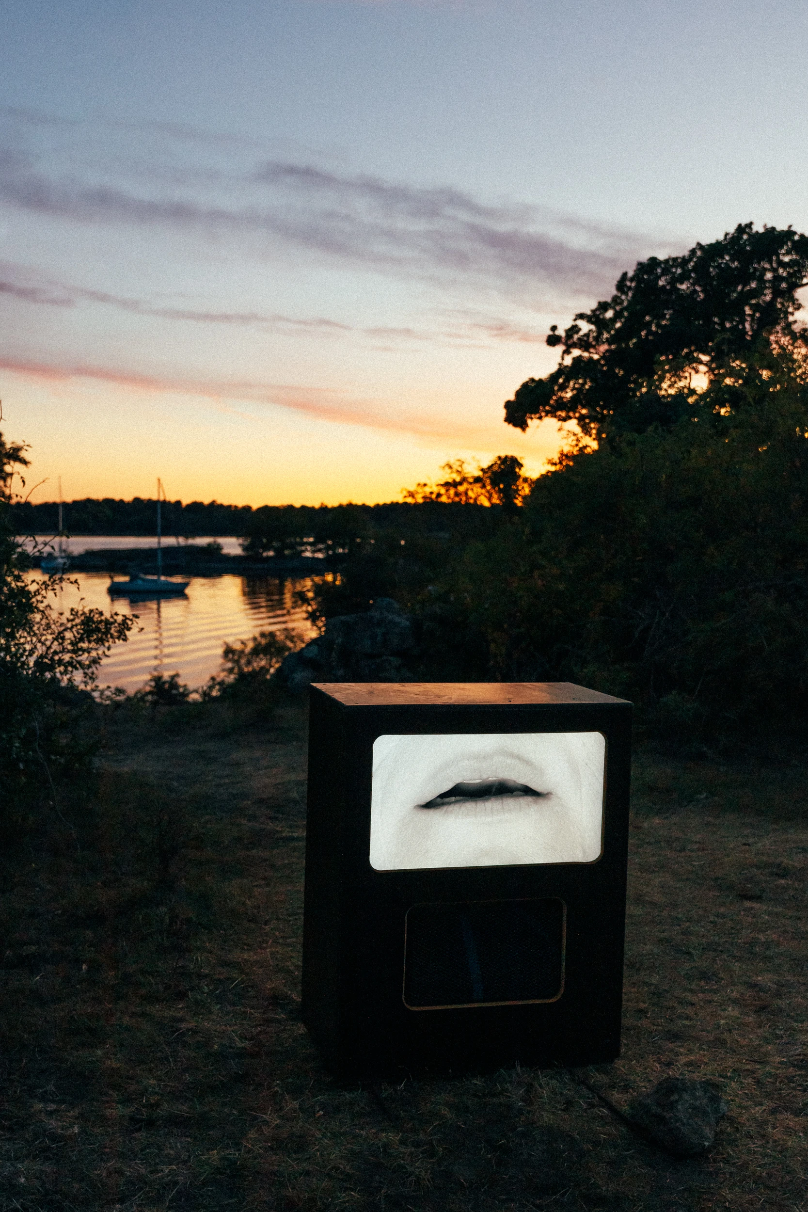A dark plinth holds a white sculpture of parted lips, facing the archipelago at dusk.